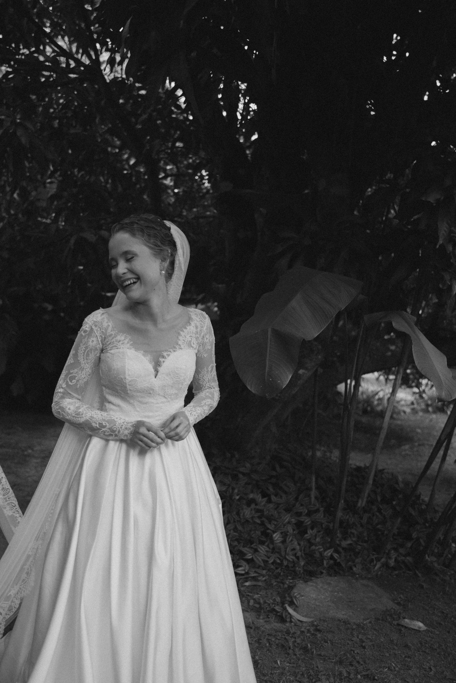 Black and white photo of bride in full-length lace wedding gown outdoors.