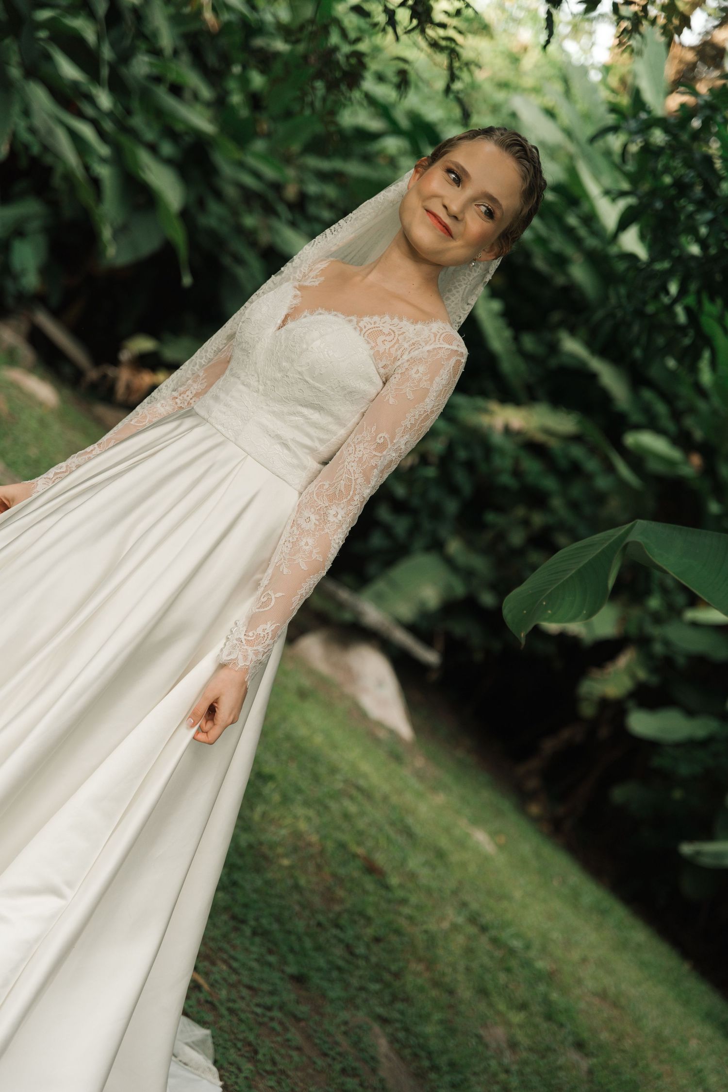 Elegant white lace wedding dress with long sleeves photographed against lush greenery in a garden setting.