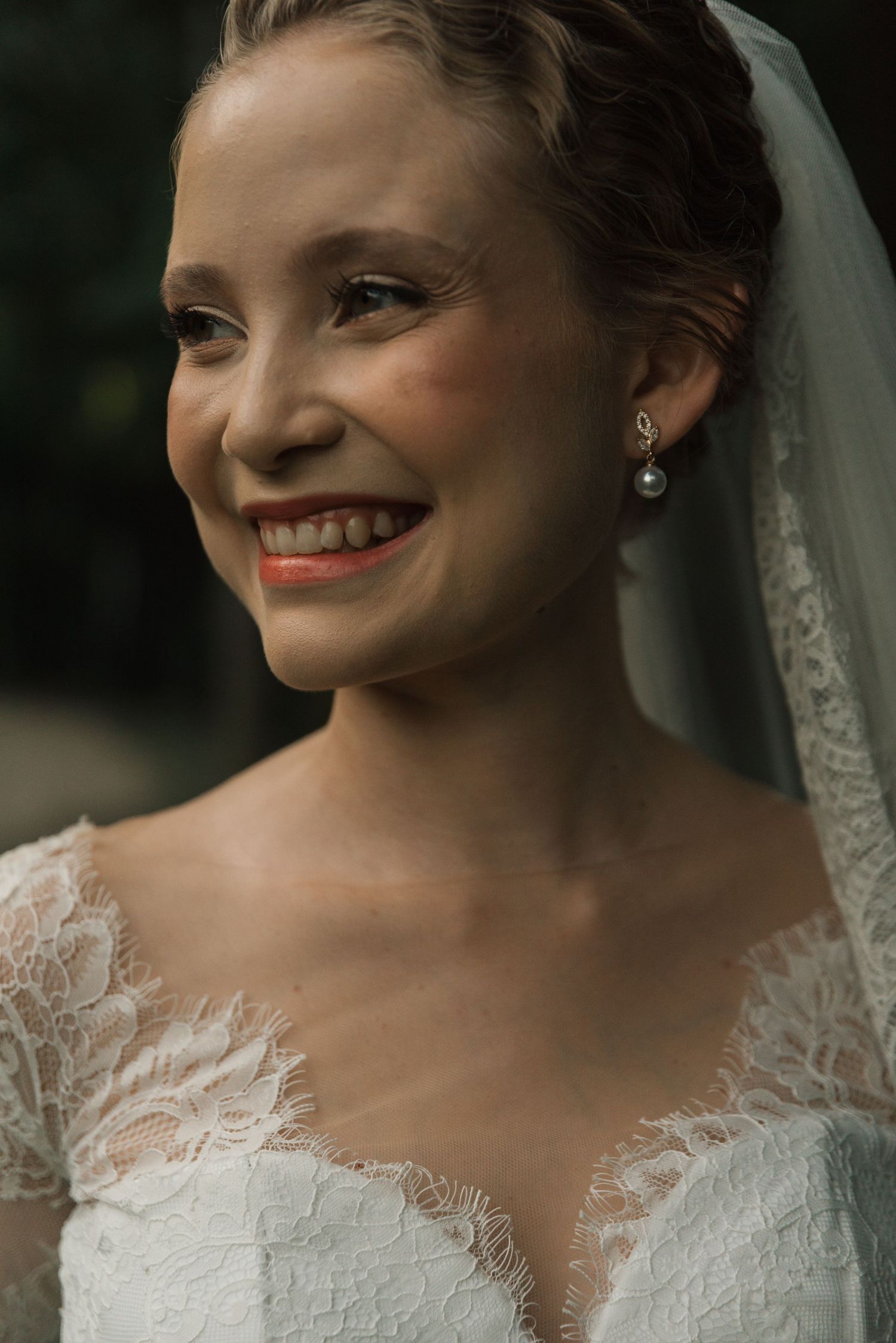 Radiant bride wearing delicate pearl earrings and lace wedding gown with a classic veil.