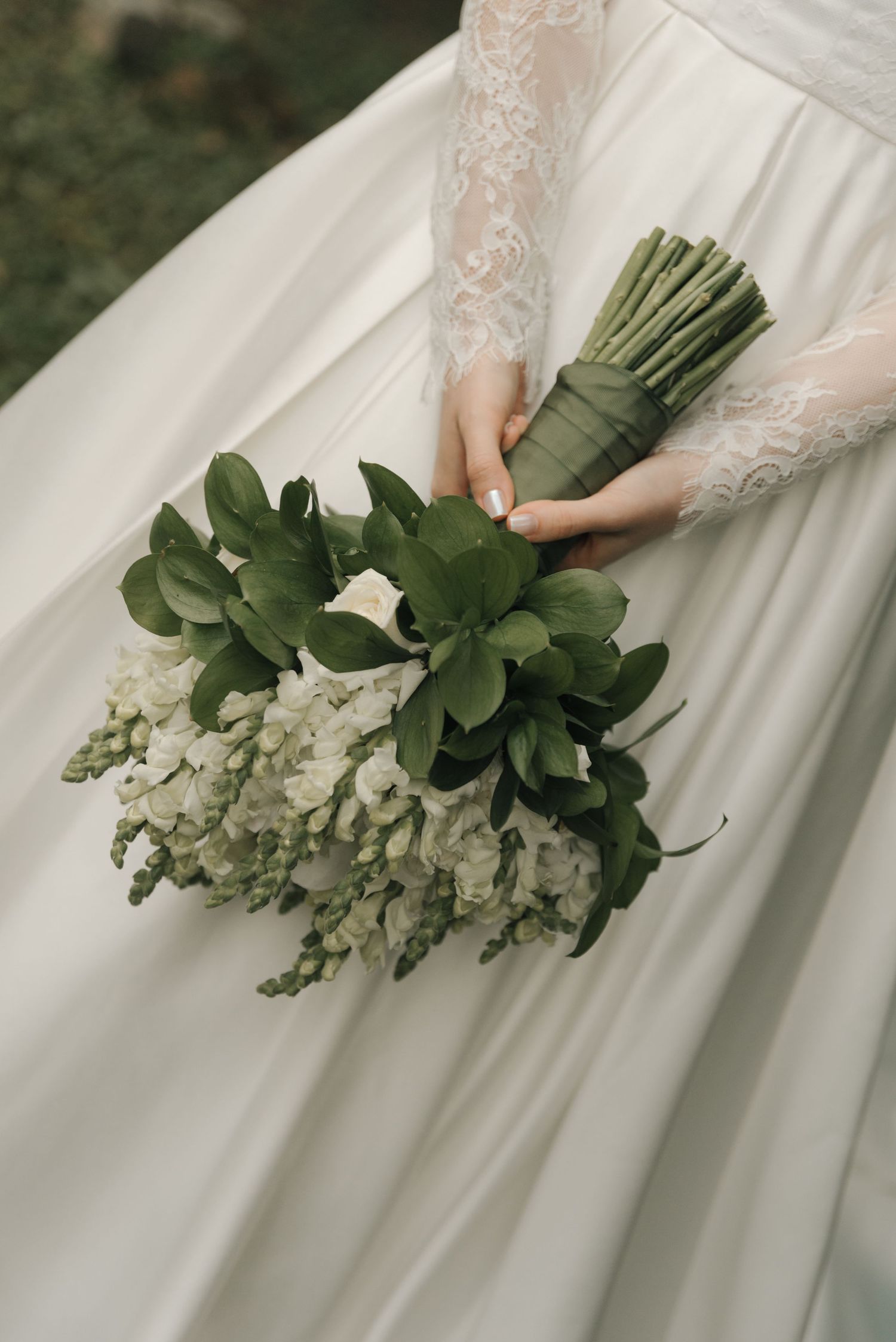 Close-up of bridal bouquet featuring white blooms and green foliage against white wedding dress.