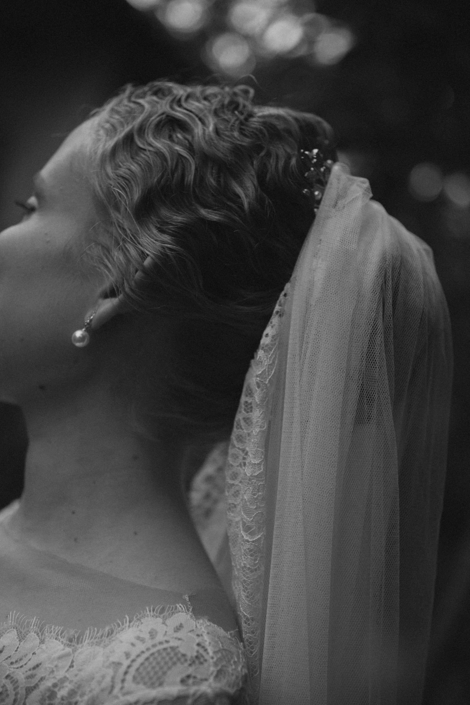 Dramatic black and white side profile of bride wearing delicate veil and lace dress.