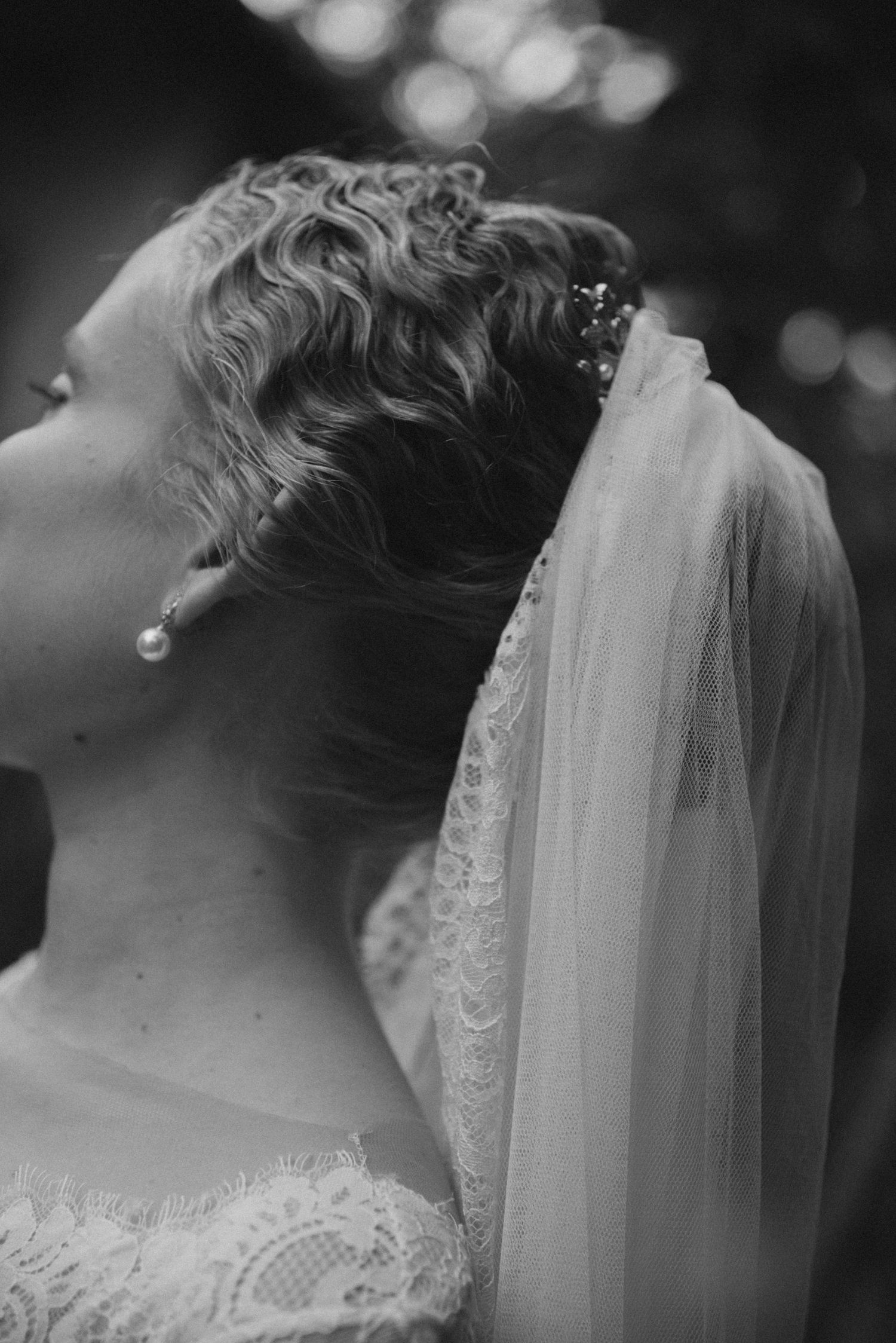 Artistic black and white profile portrait of bride with vintage-style veil and curled hair.
