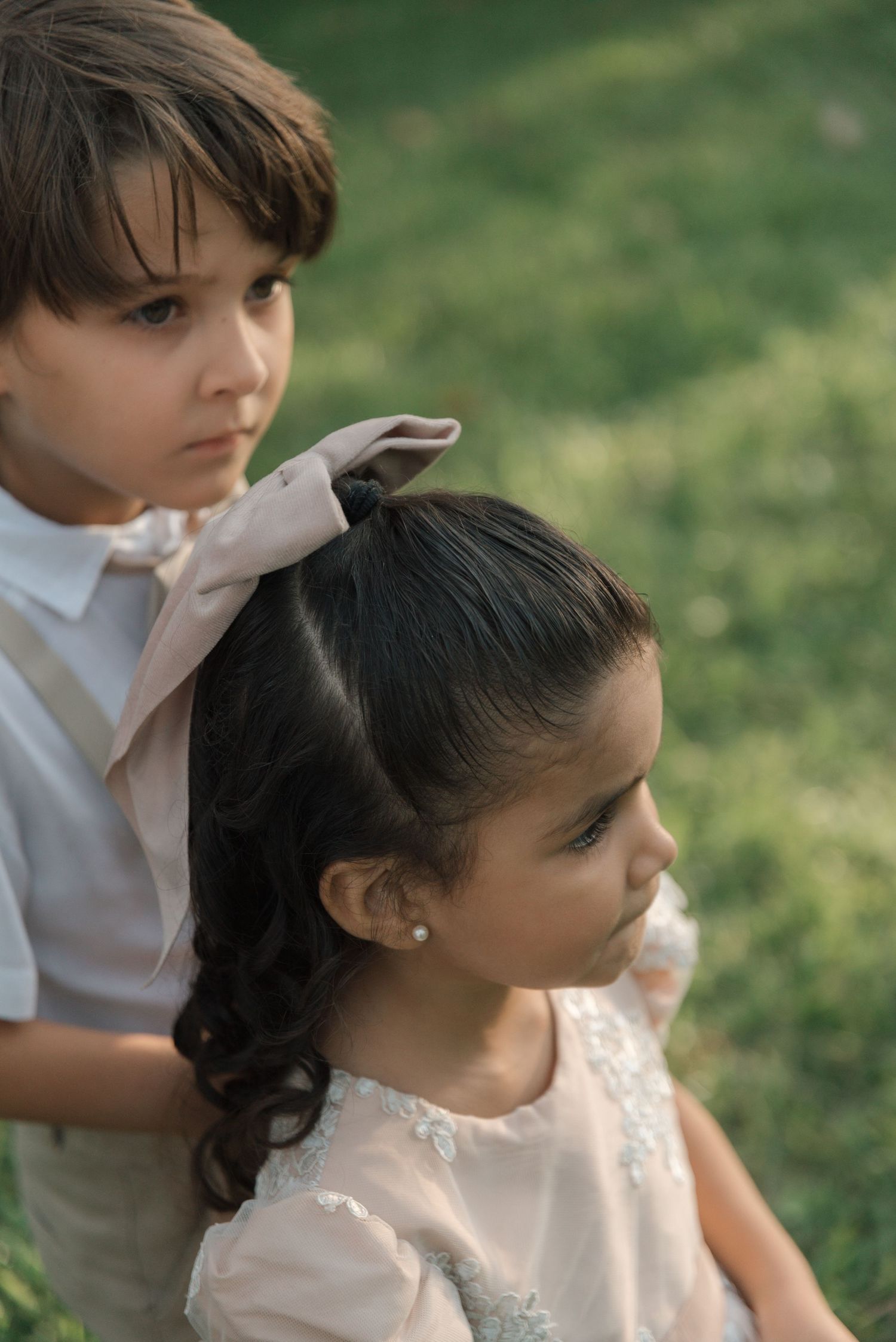 Two young wedding attendants in formal attire stand together in a garden setting at dusk.