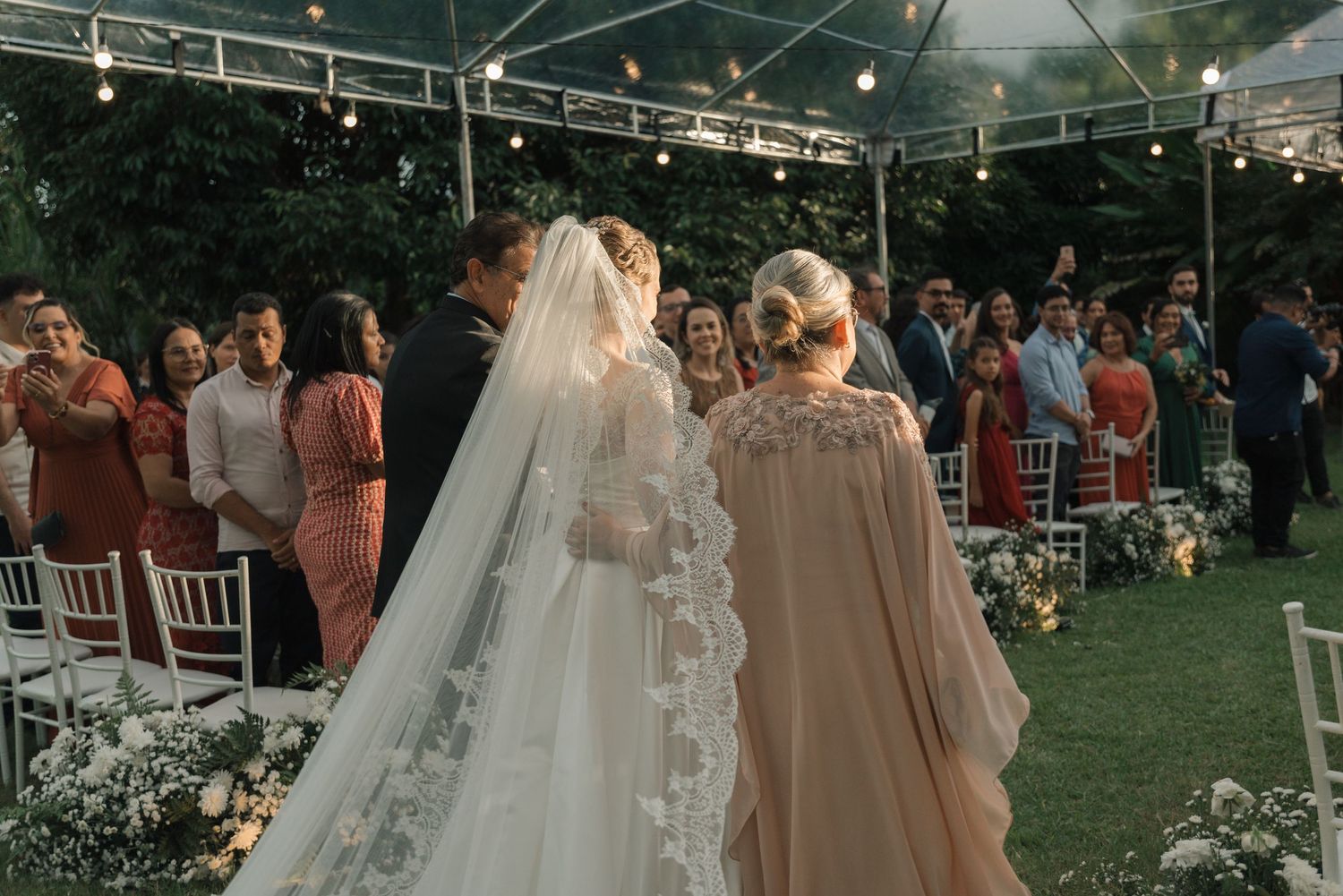 Wedding ceremony under clear tent with floral decorations and white chairs.