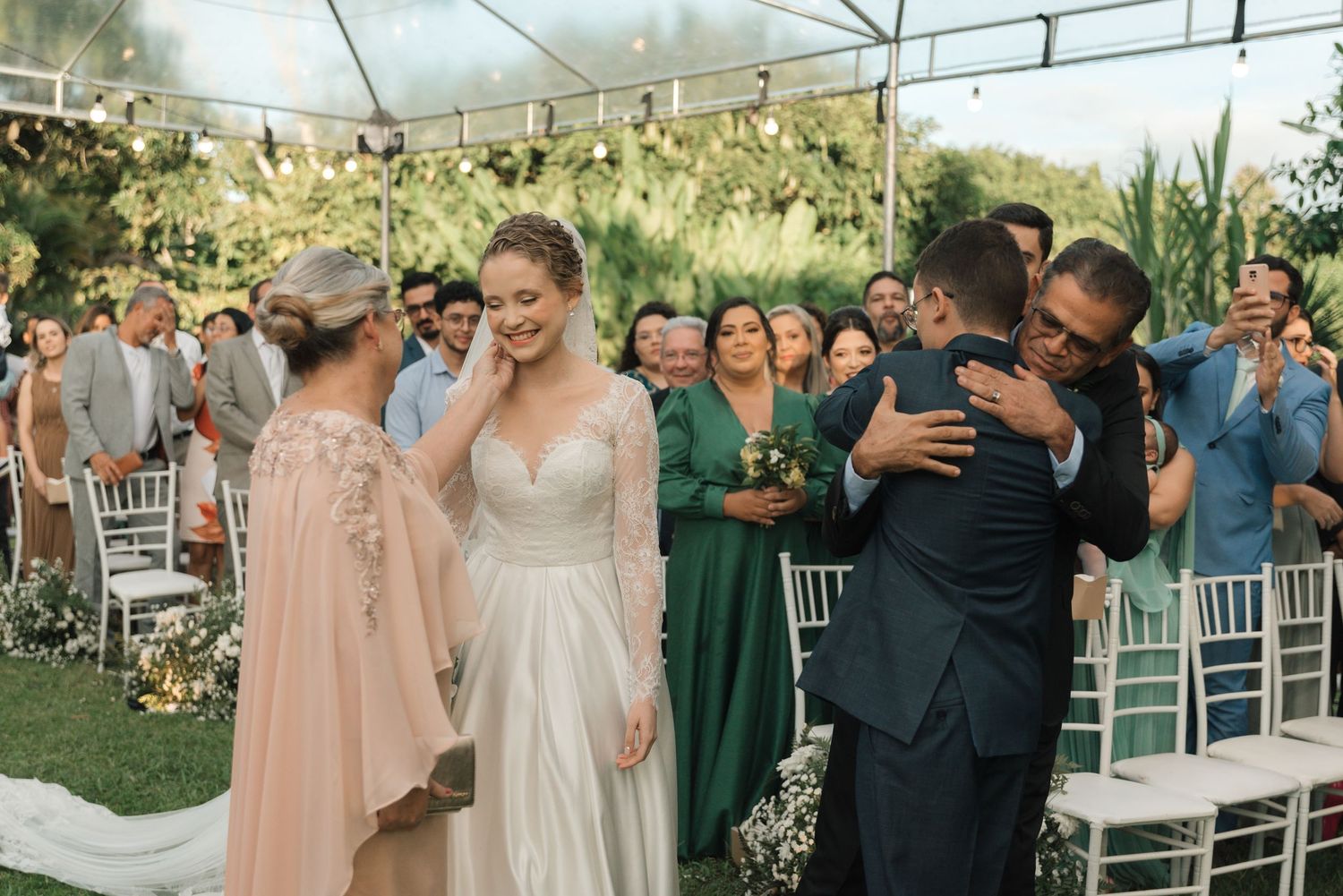 Joyful wedding ceremony scene under a tent with guests in emerald green dresses celebrating the newlyweds.