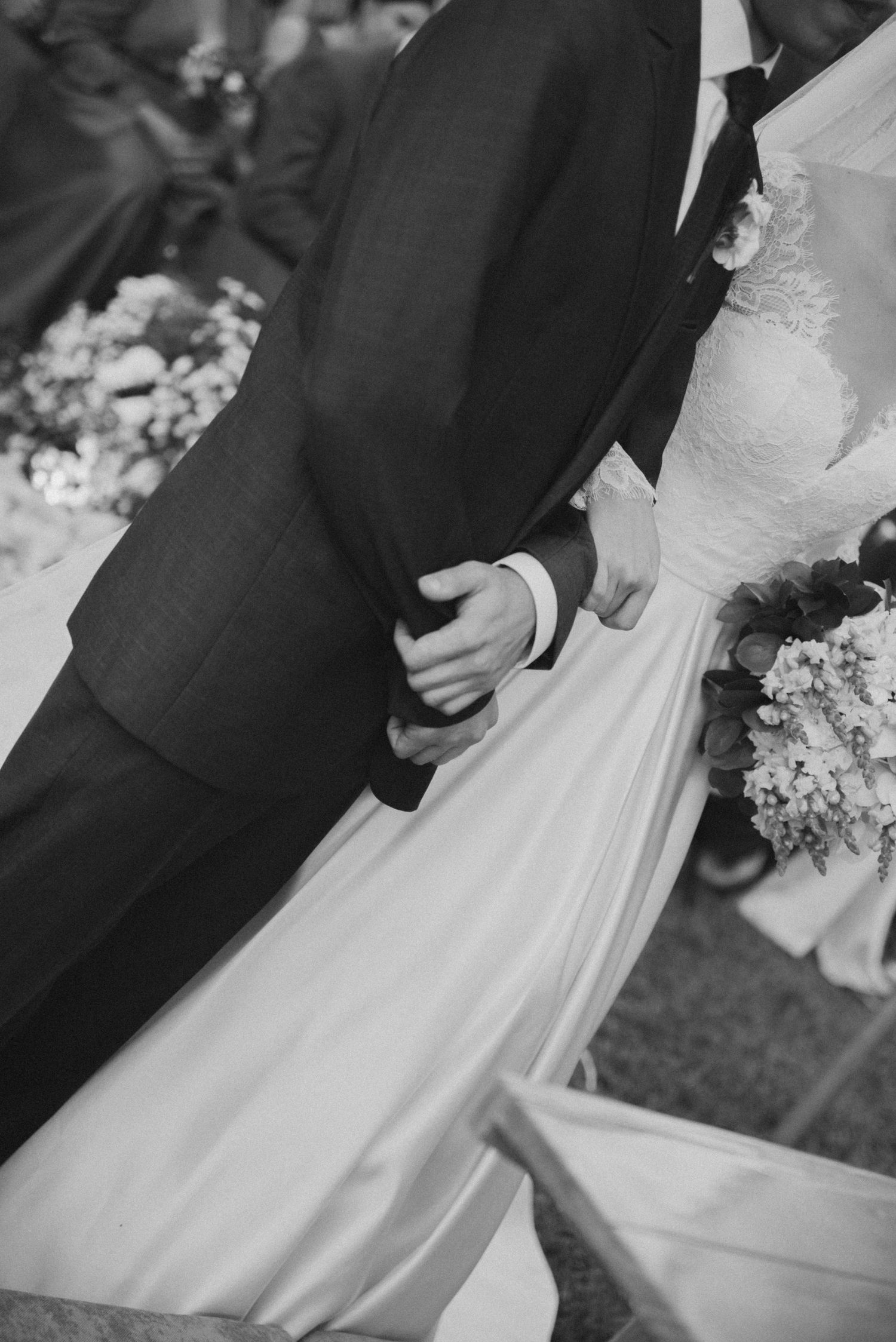 Black and white close-up of bride and groom holding hands during wedding ceremony.