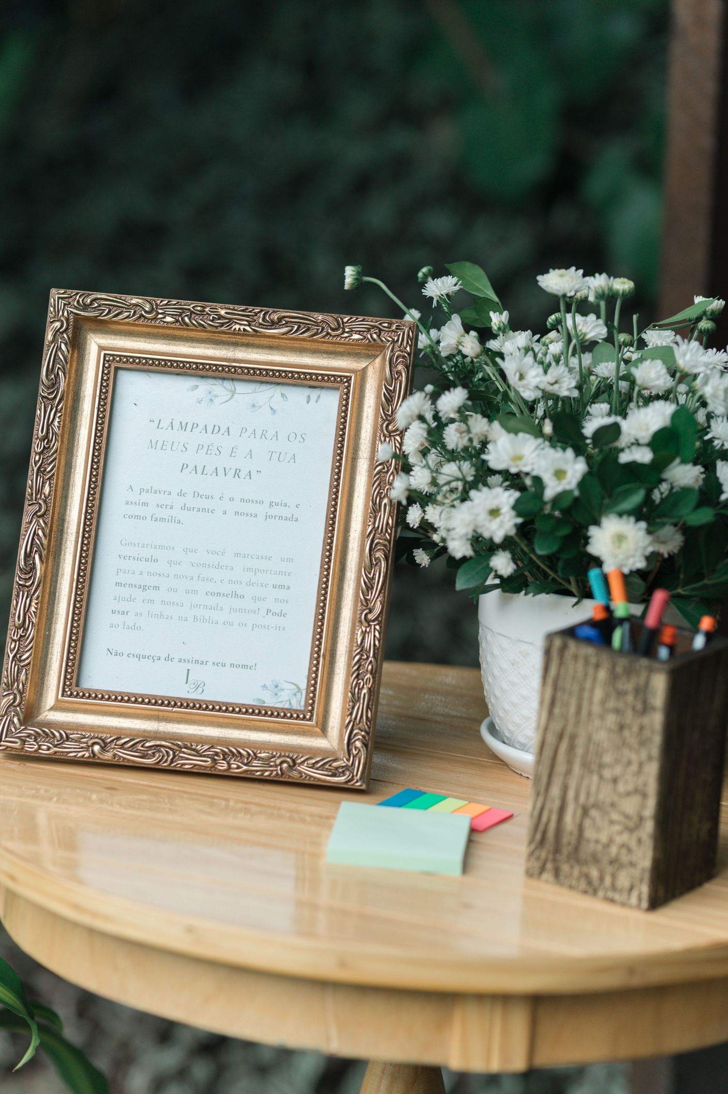 Ornate gold frame with wedding details and white floral arrangement on wooden table.