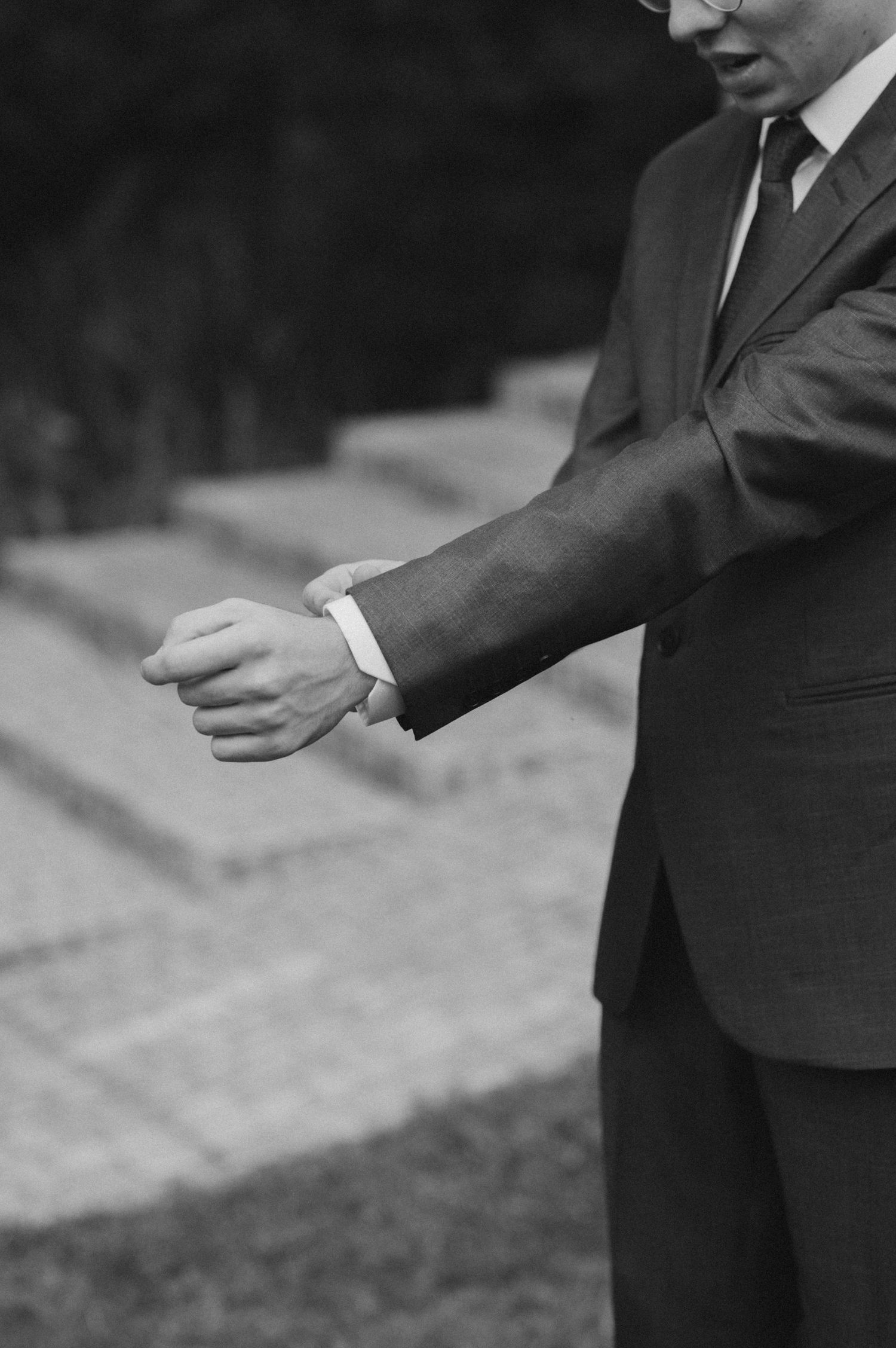 Black and white photo of groom checking time on wristwatch before ceremony.