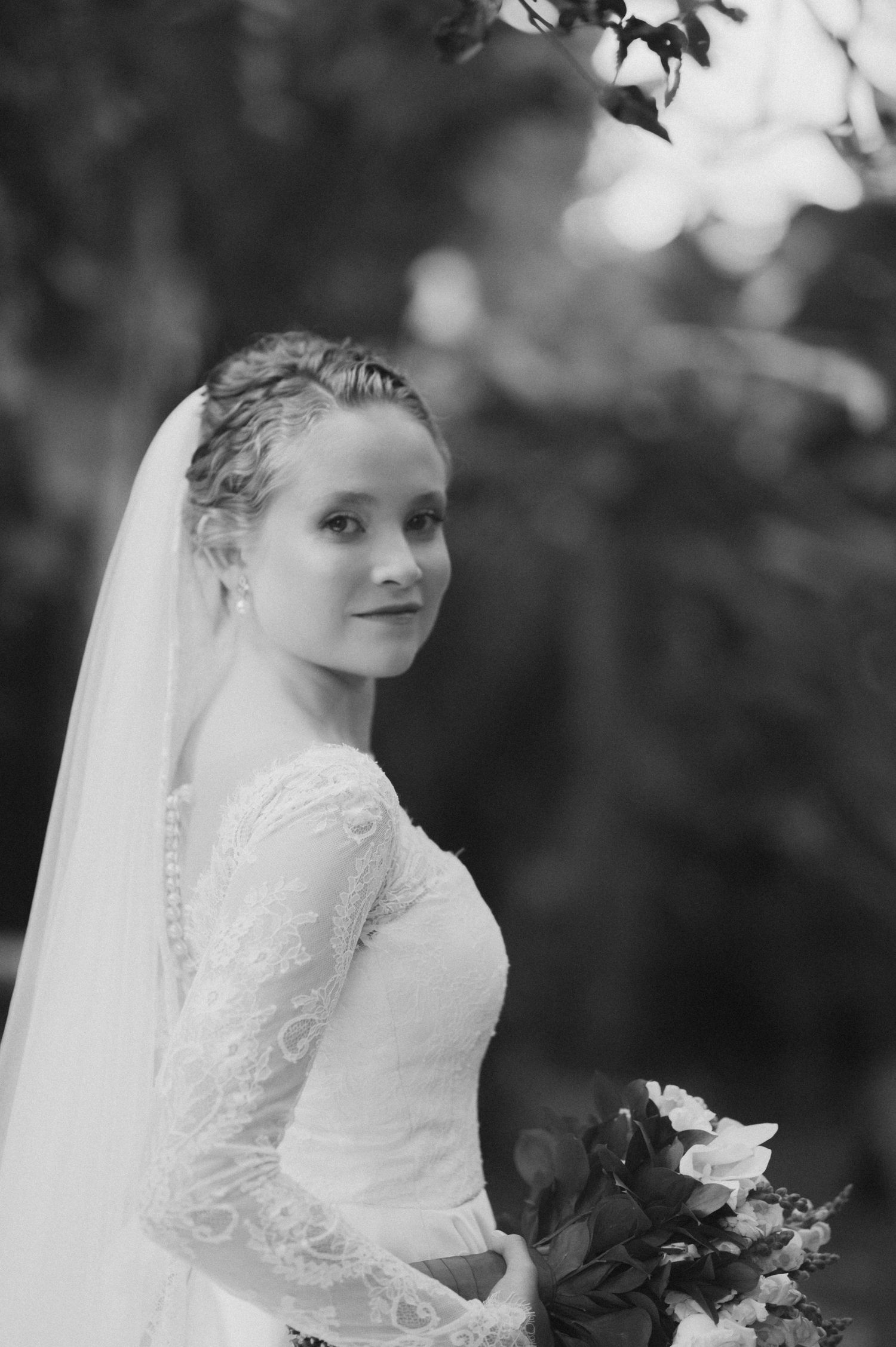 A black and white bridal portrait showing a bride in a long-sleeved lace dress holding a bouquet.