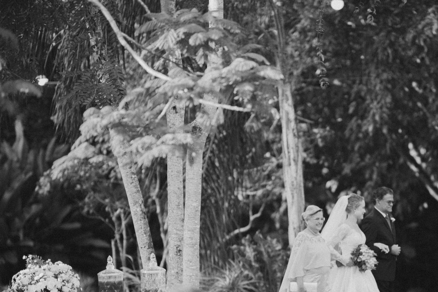 A black and white wedding photo capturing a couple under a decorated outdoor arch.