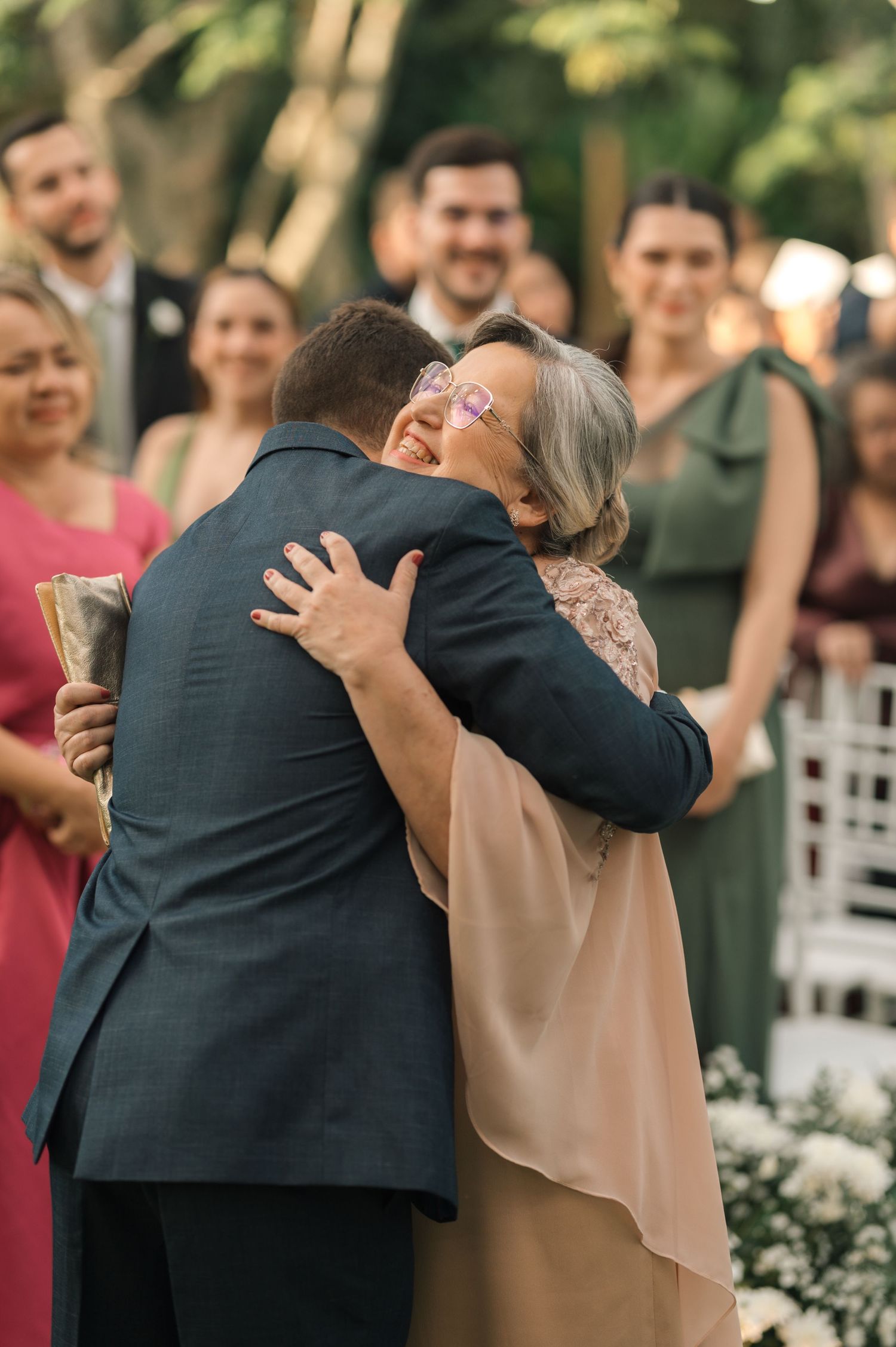 Touching embrace between wedding guests during outdoor celebration with guests looking on.