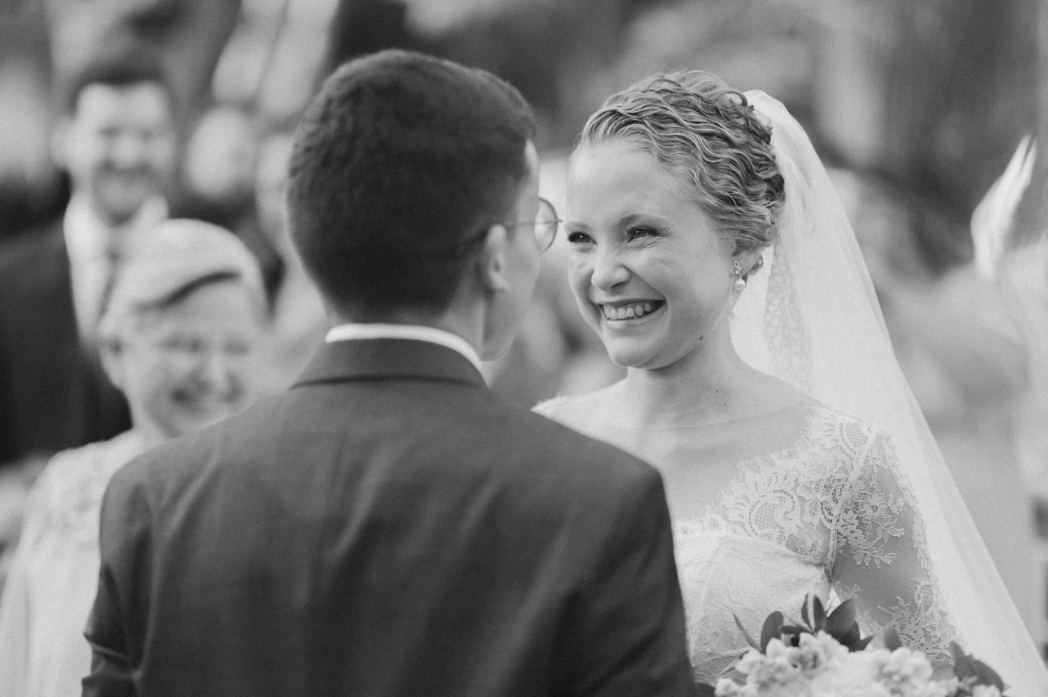 Black and white photo capturing intimate wedding ceremony moment with smiling bride.