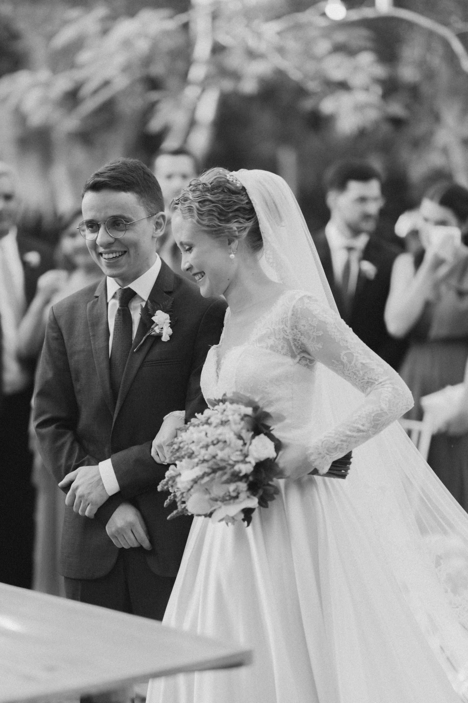 Black and white photo of couple laughing during wedding ceremony outdoors.