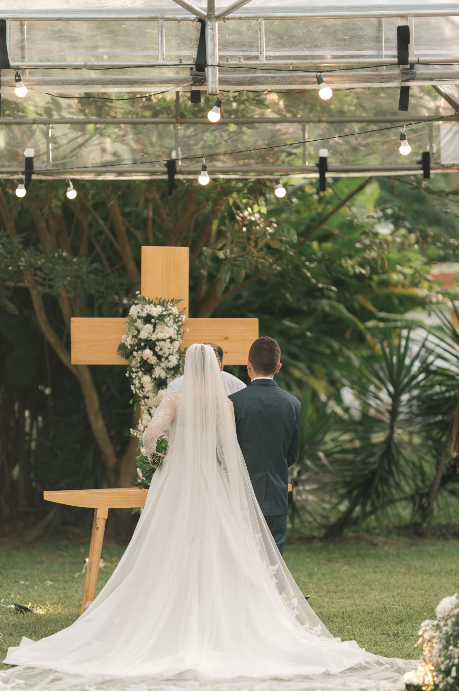 Wedding ceremony setup with wooden cross and string lights as couple faces altar.