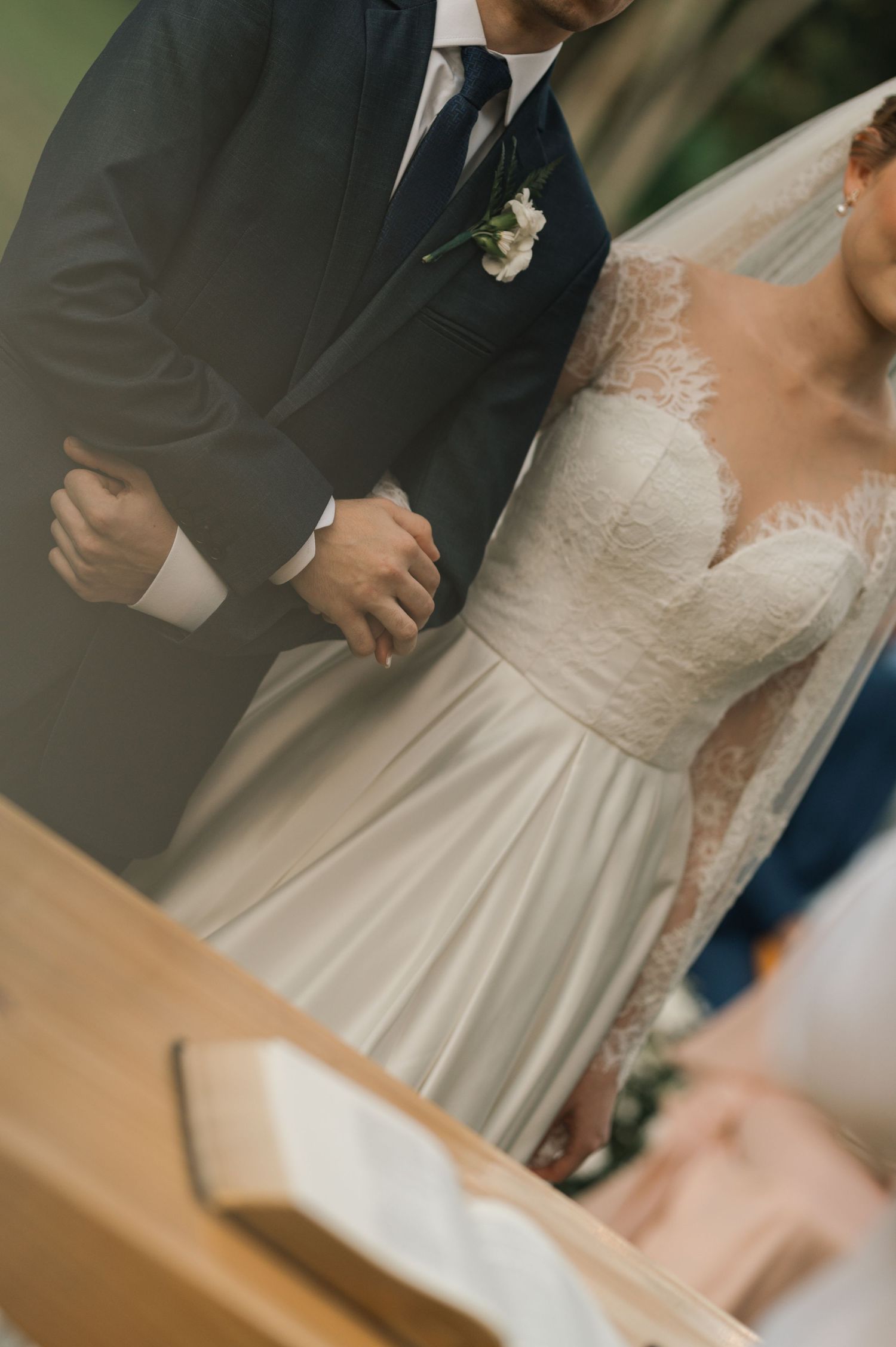Details of a bride's lace wedding dress and groom's suit during the ceremony.