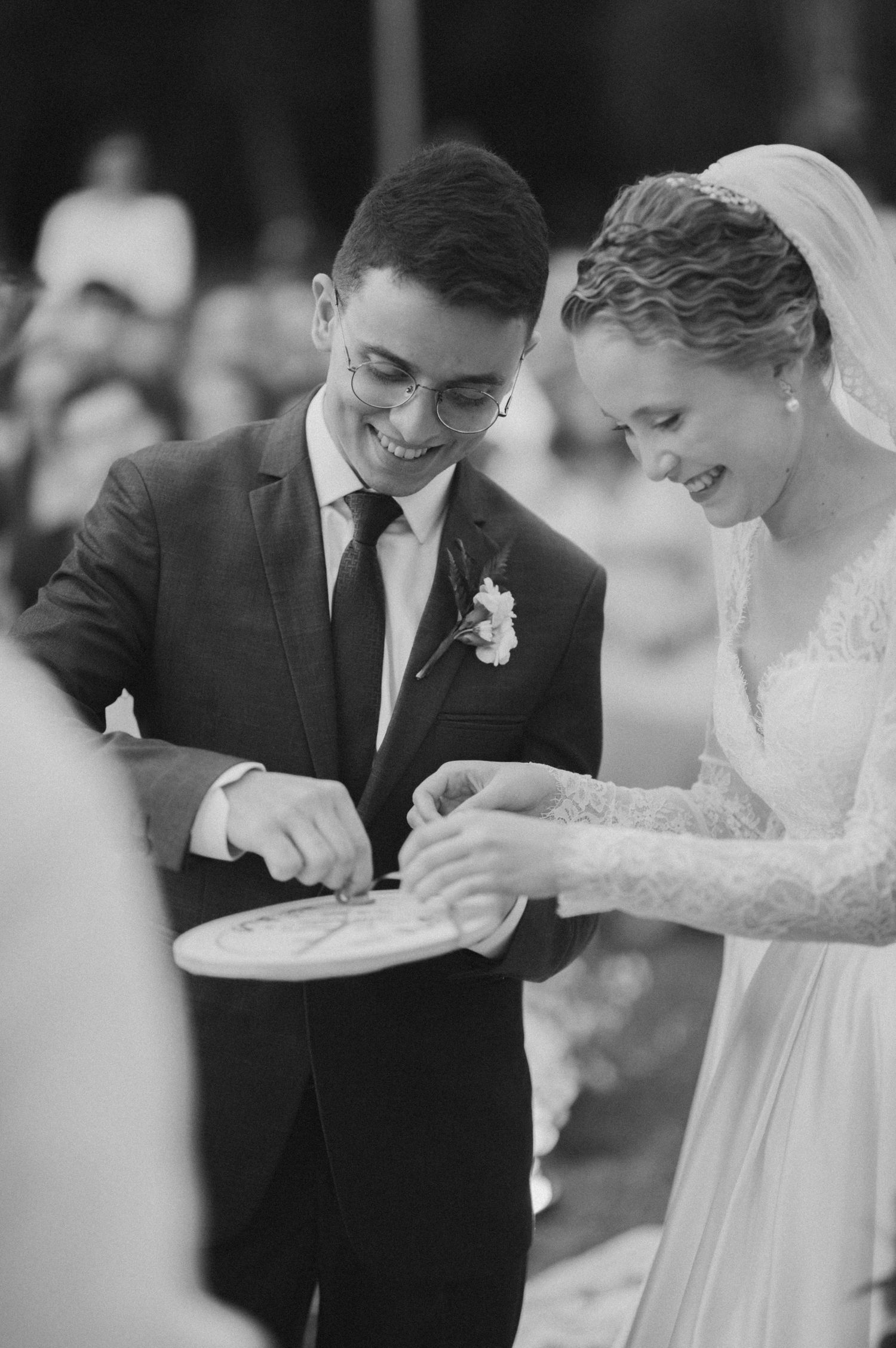 A joyful couple exchanges rings during their outdoor wedding ceremony, with the bride in lace and groom in a dark suit.