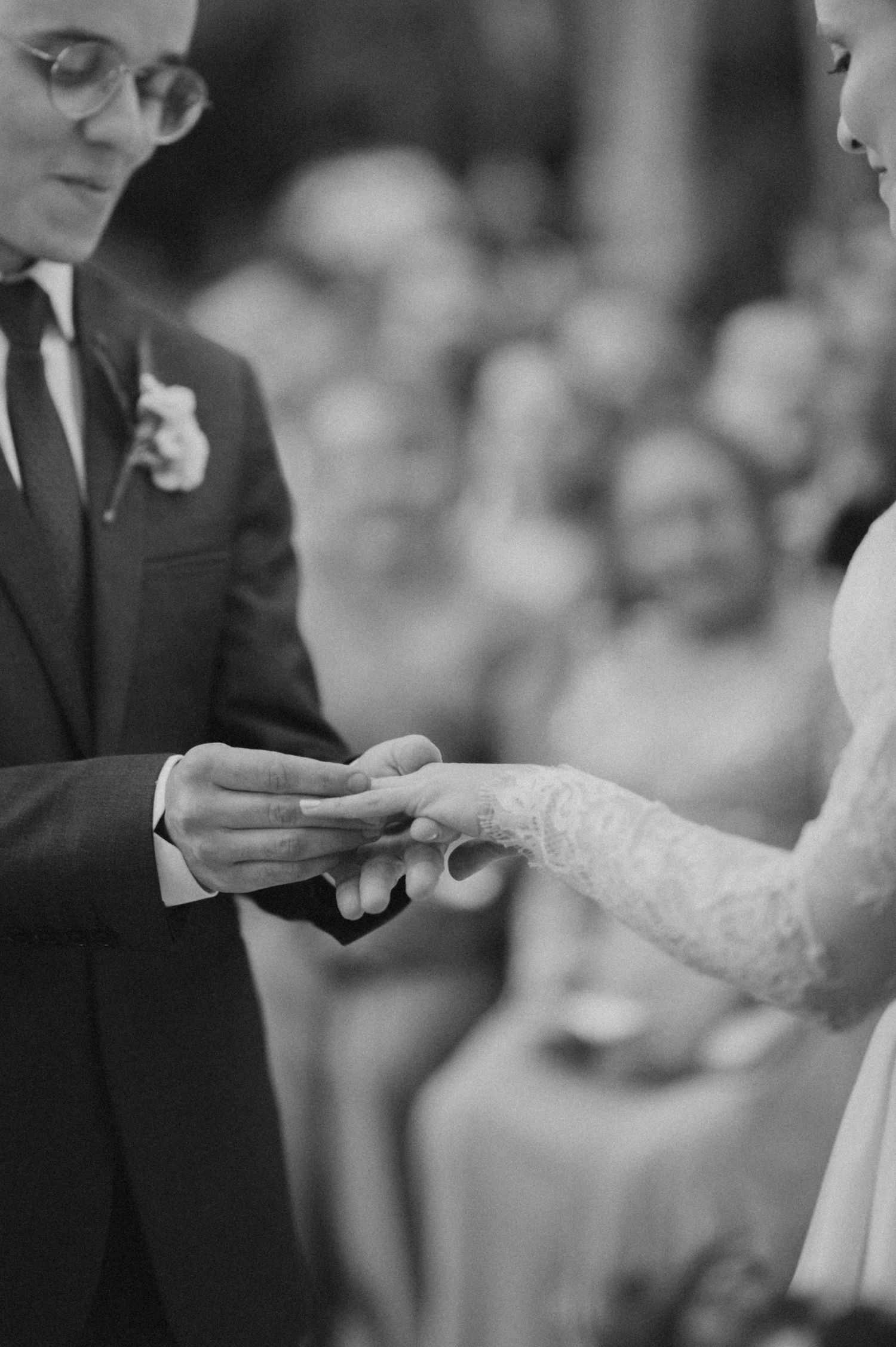 A close-up shot of wedding ring exchange with the bride's lace sleeve visible.