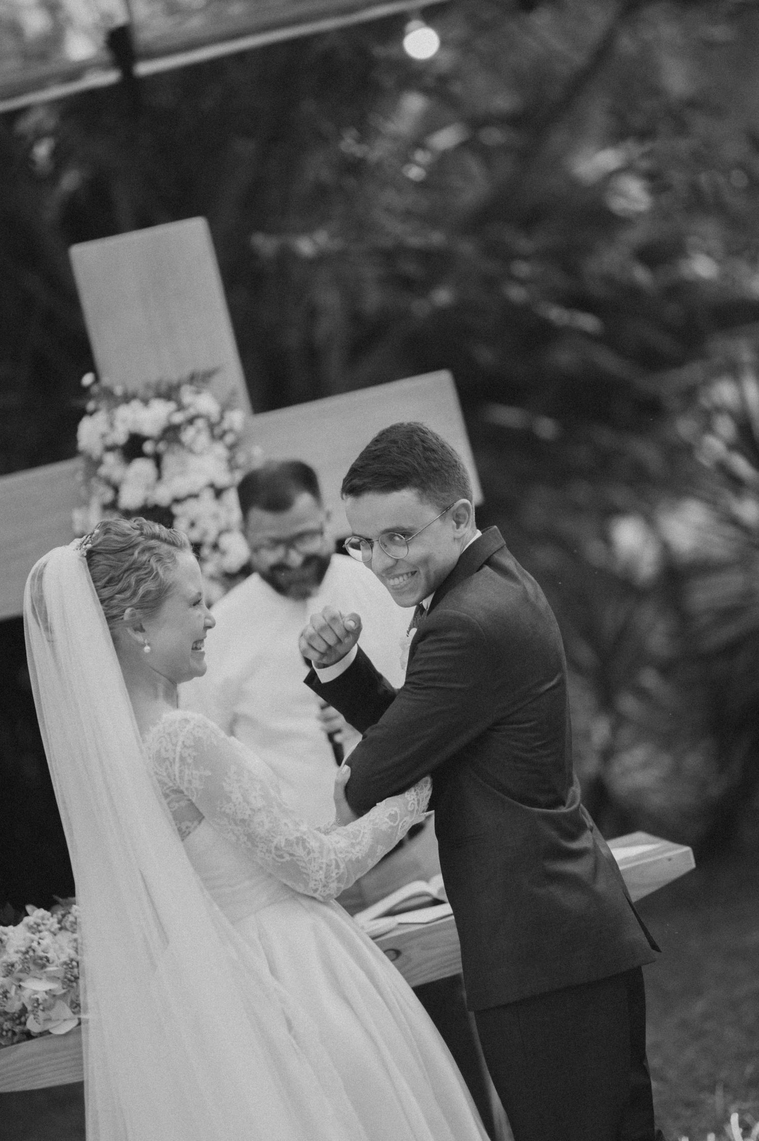 Happy couple shares a tender moment at their outdoor wedding with a wooden cross in the background.