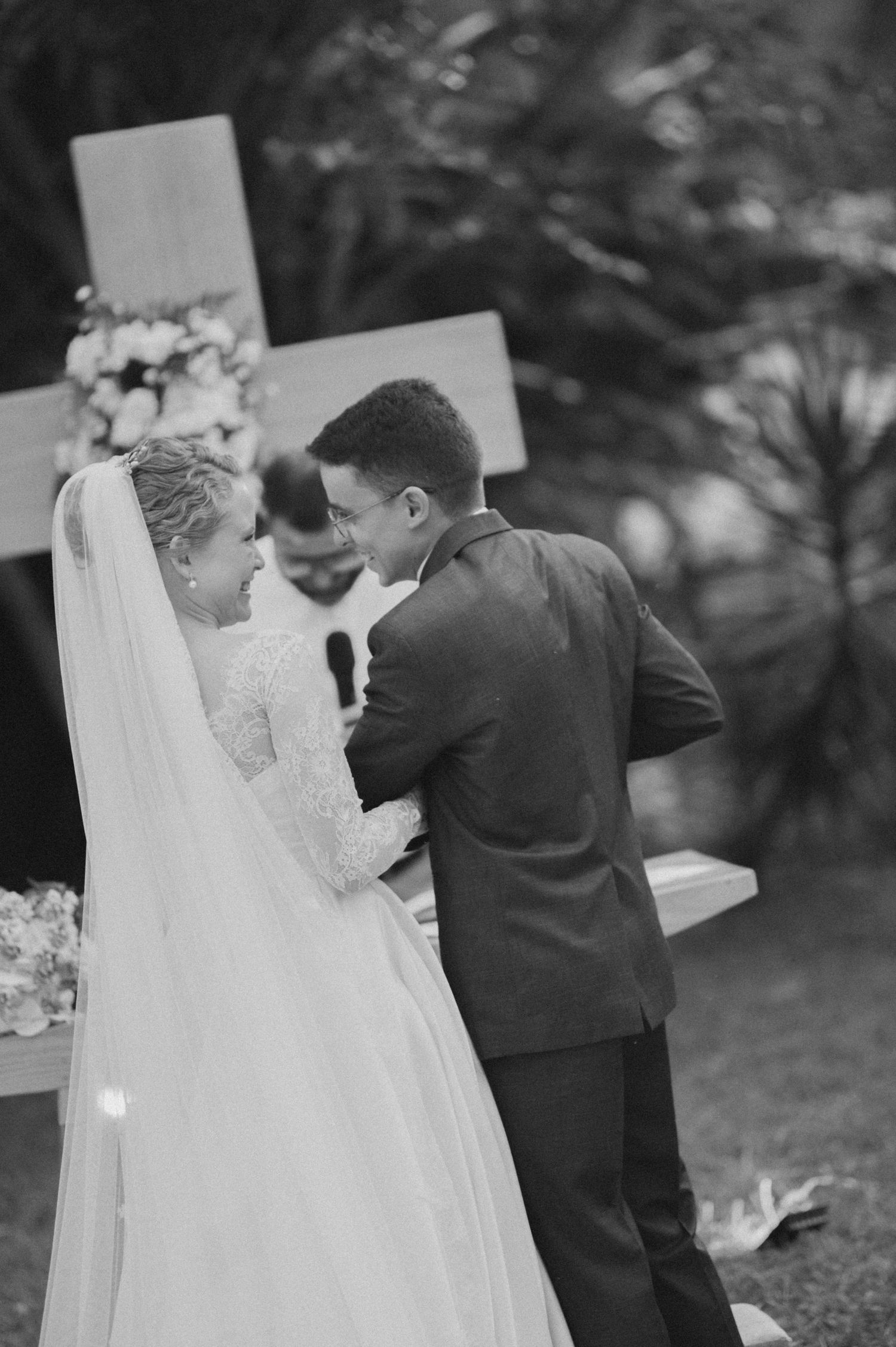 Black and white capture of a wedding couple's intimate moment in front of a cross during their ceremony.