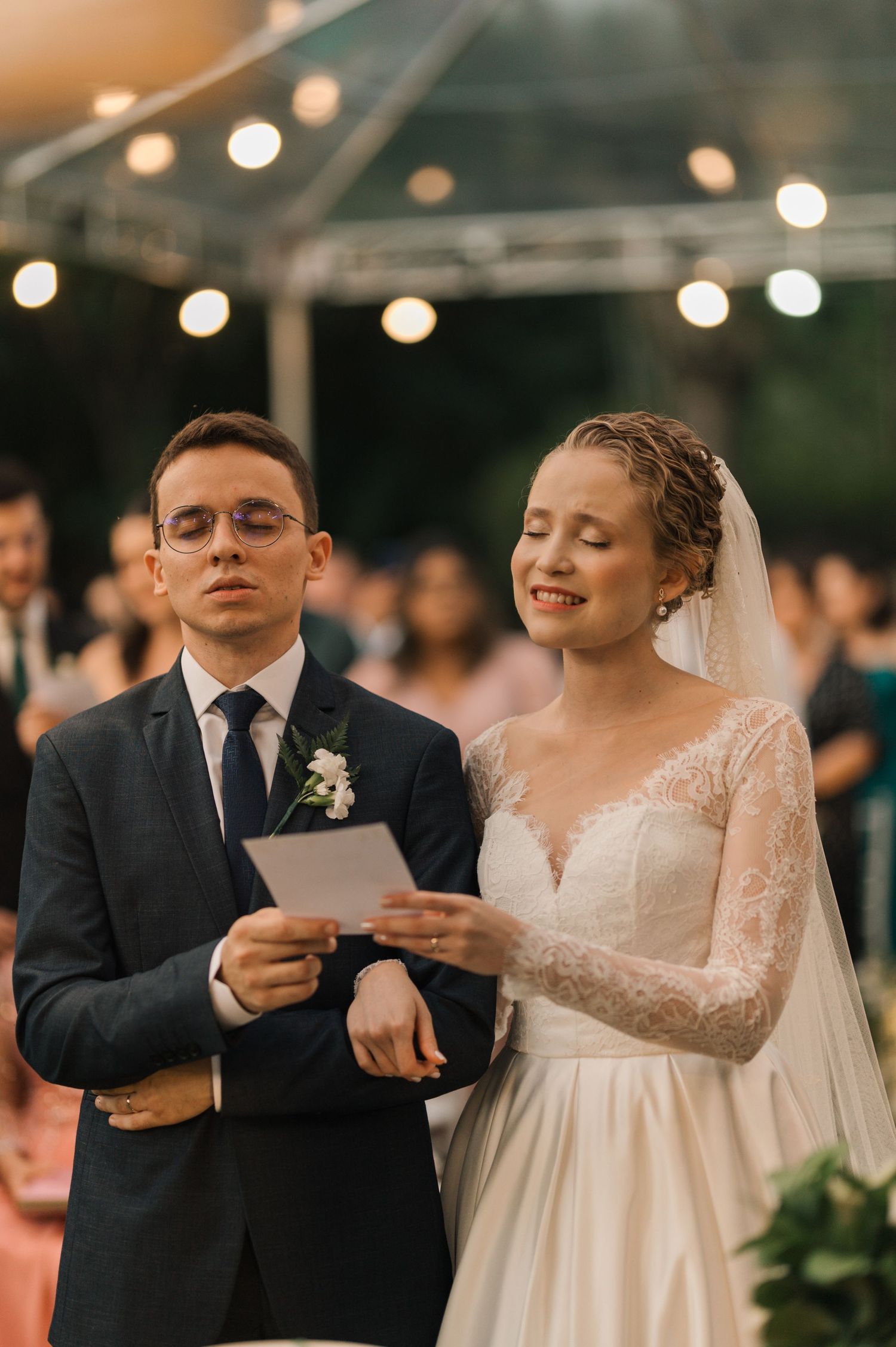 Couple reads ceremony notes together under twinkling lights at their outdoor wedding.