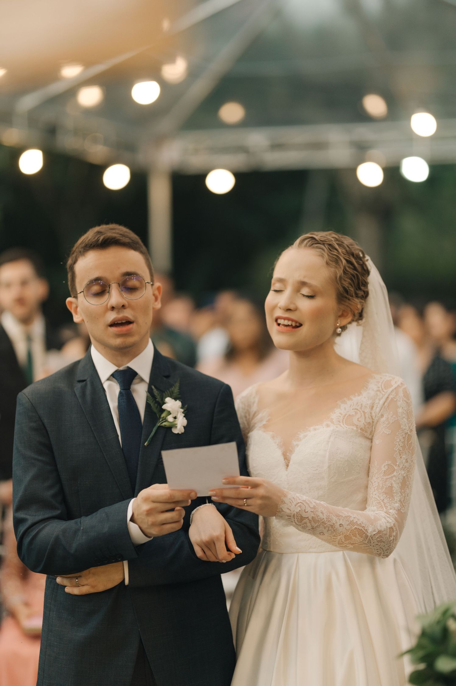 Couple reads from a paper during their evening wedding ceremony under string lights.