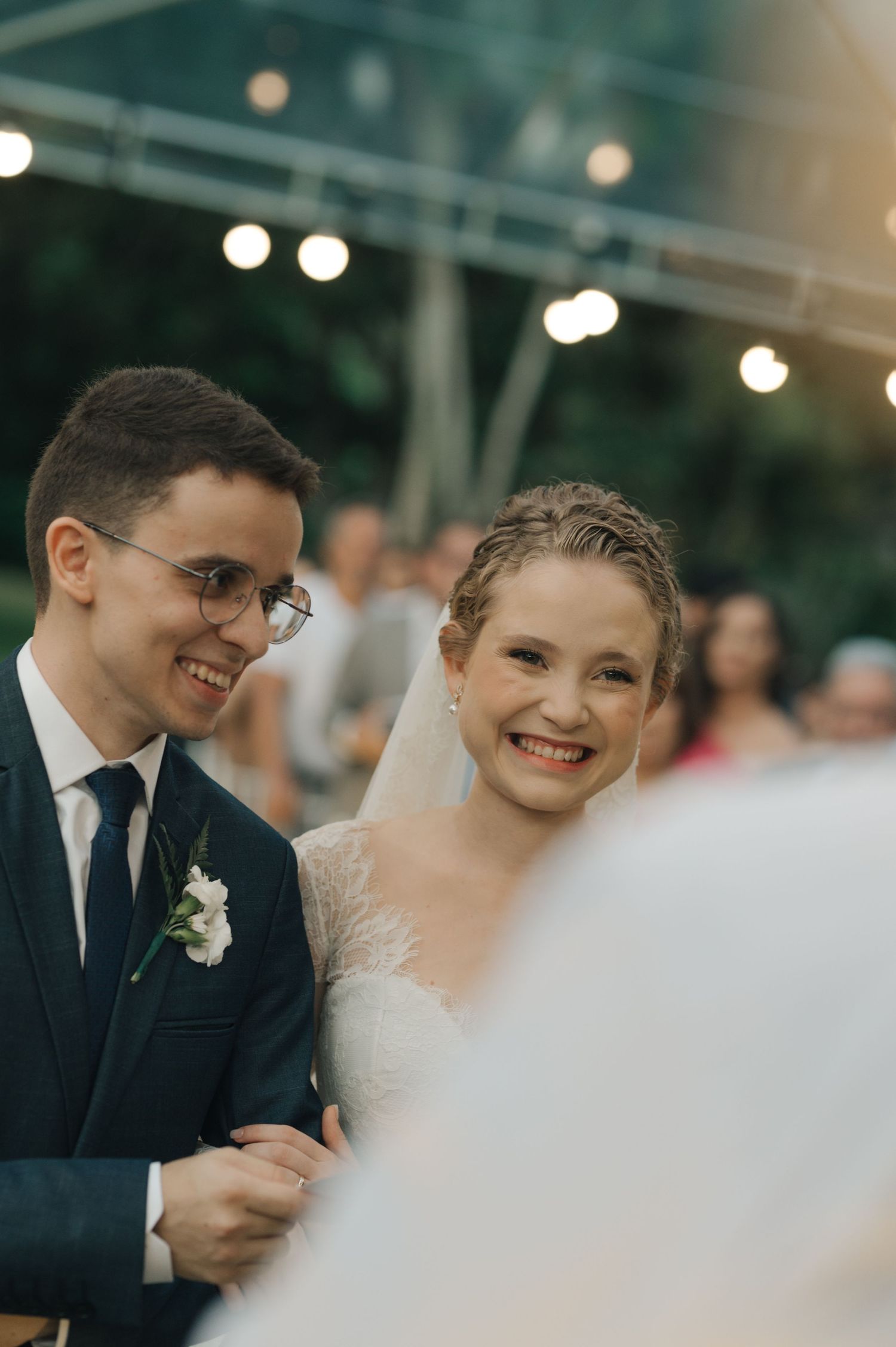 A joyful couple smiles during their wedding ceremony under twinkling outdoor lights.