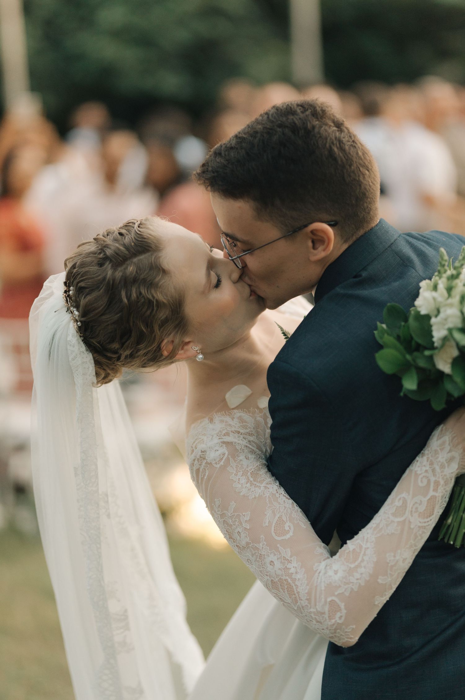 Intimate wedding kiss captured under string lights at outdoor reception.
