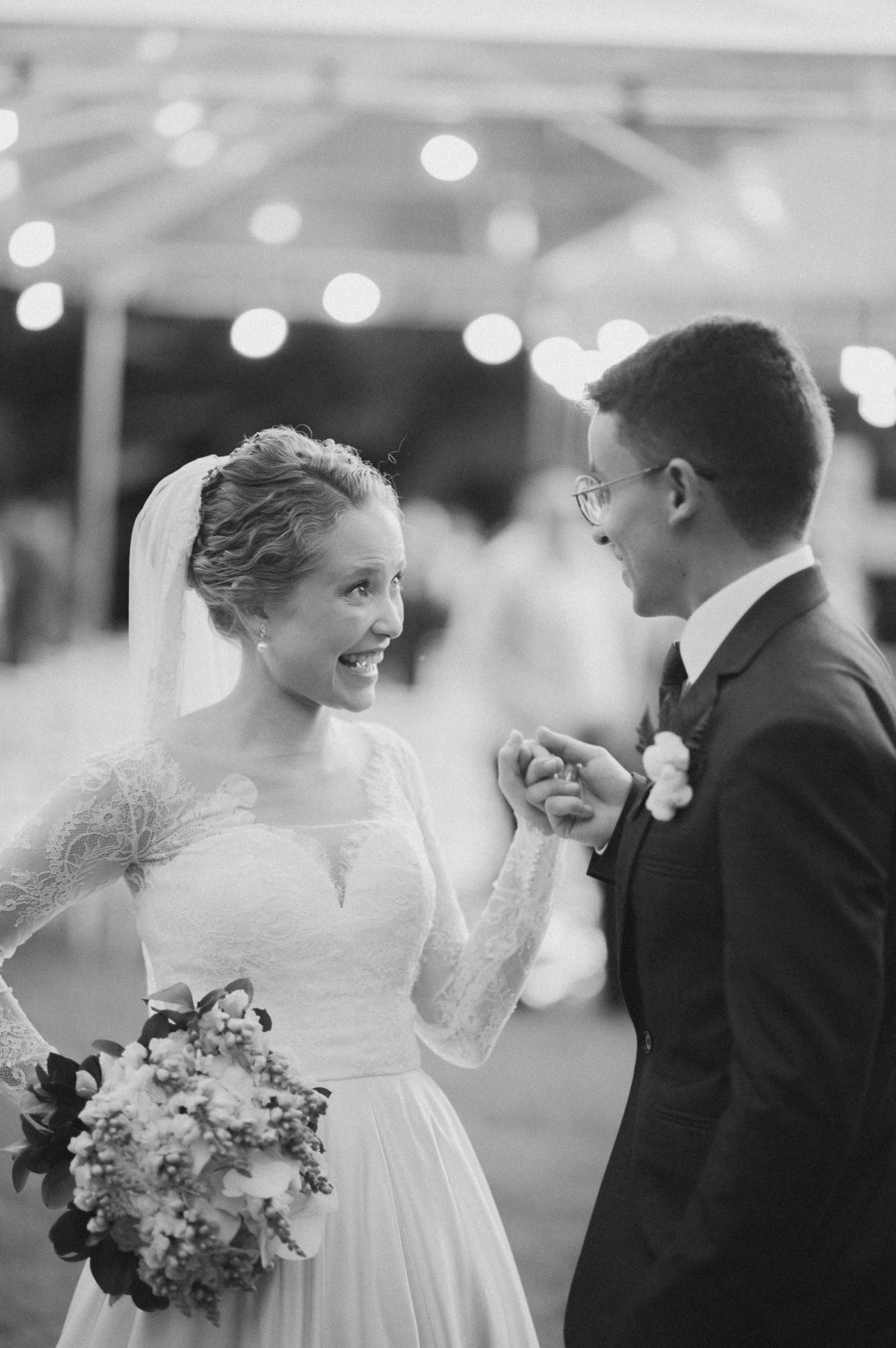 Black and white photo of bride and groom sharing a lighthearted moment with bouquet.