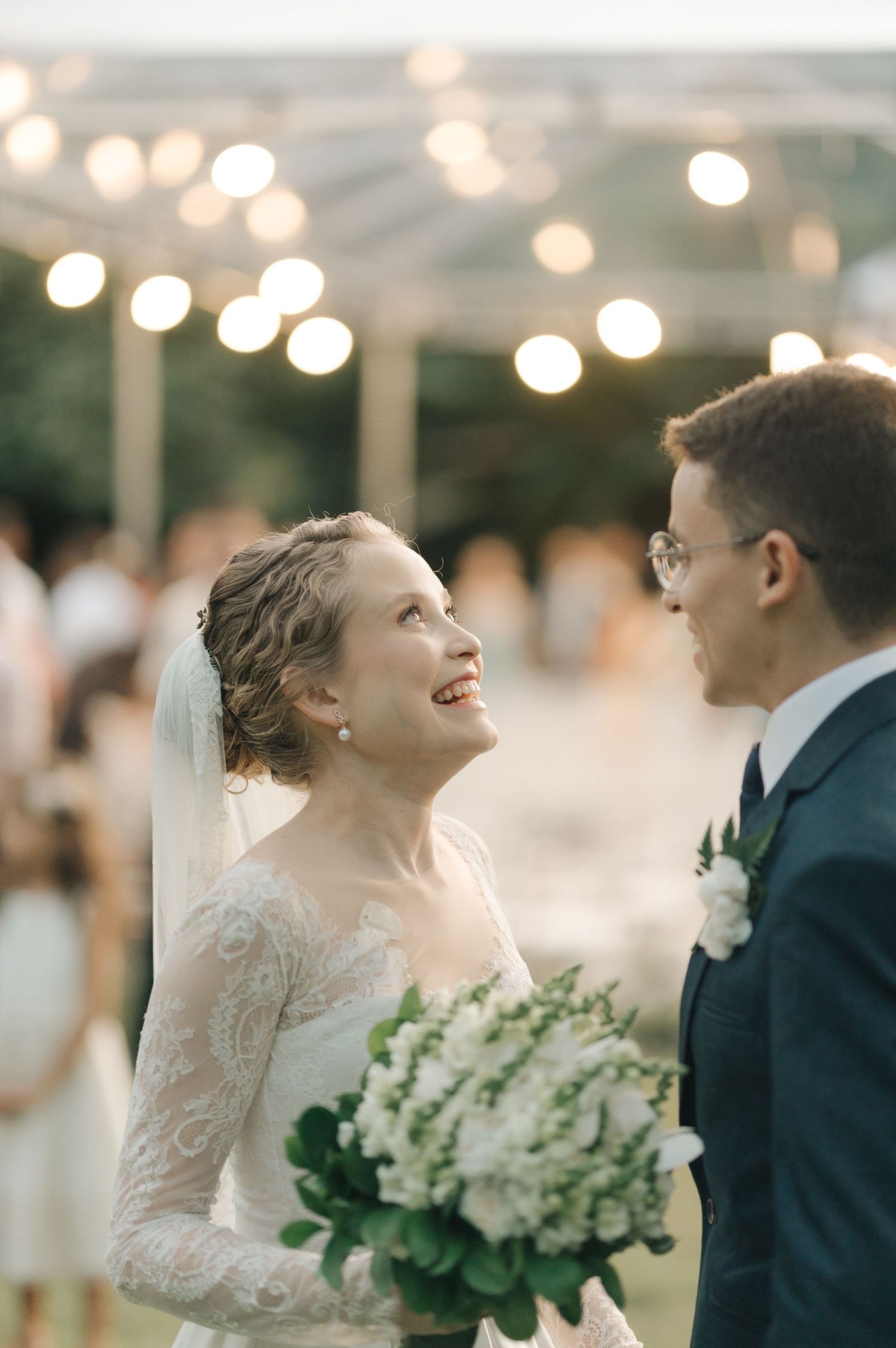 Candid moment of bride looking up at groom under glowing reception lights.
