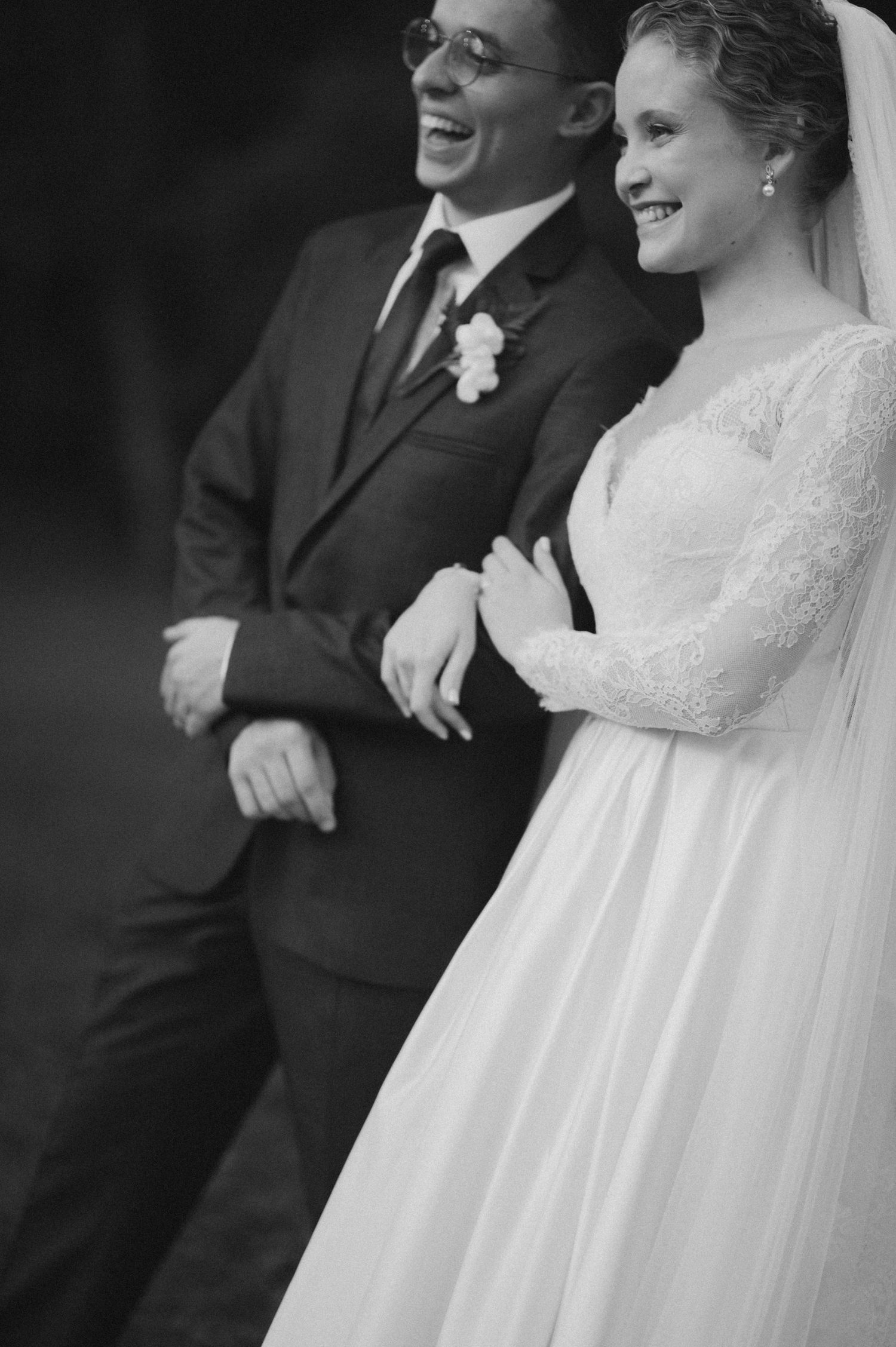 Black and white portrait of newlyweds laughing together during their outdoor wedding celebration.