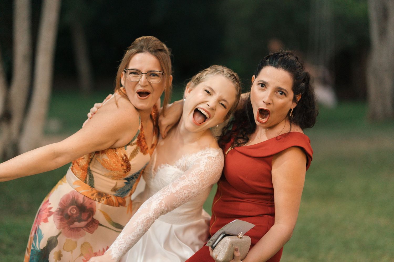 Three wedding guests share an energetic moment of laughter and excitement at an outdoor celebration.