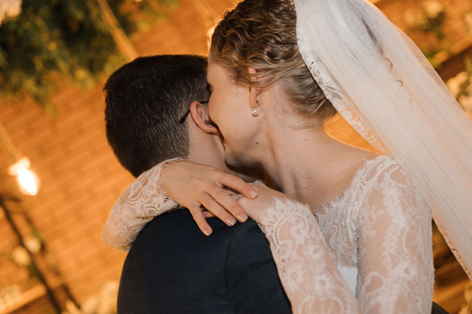 A romantic evening kiss between newlyweds under warm lighting and greenery.