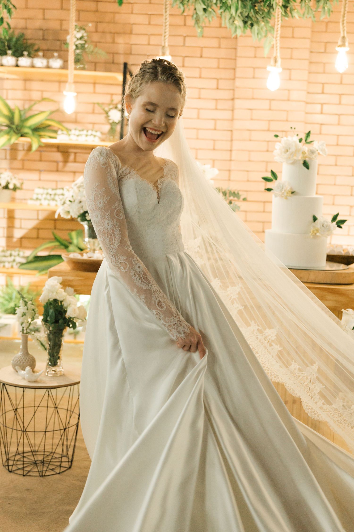 A bride twirls in her long-sleeved lace wedding gown in front of a decorative brick wall setting.