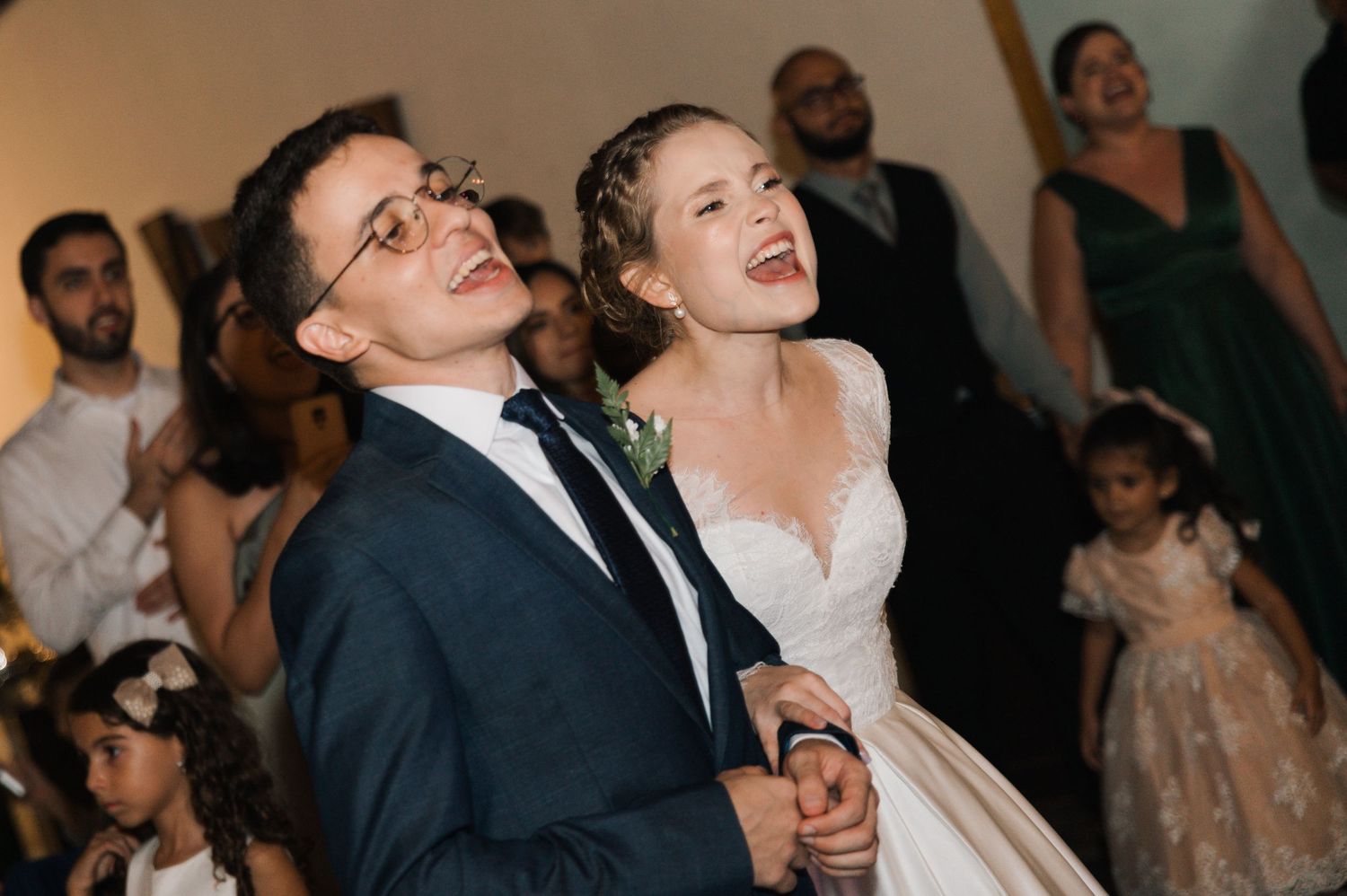 Newlyweds share an exuberant laugh during their wedding reception surrounded by celebrating guests.