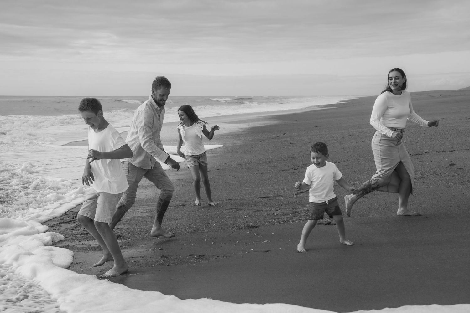 family running away from waves on Mananui Beach south of Hokitika in black and white