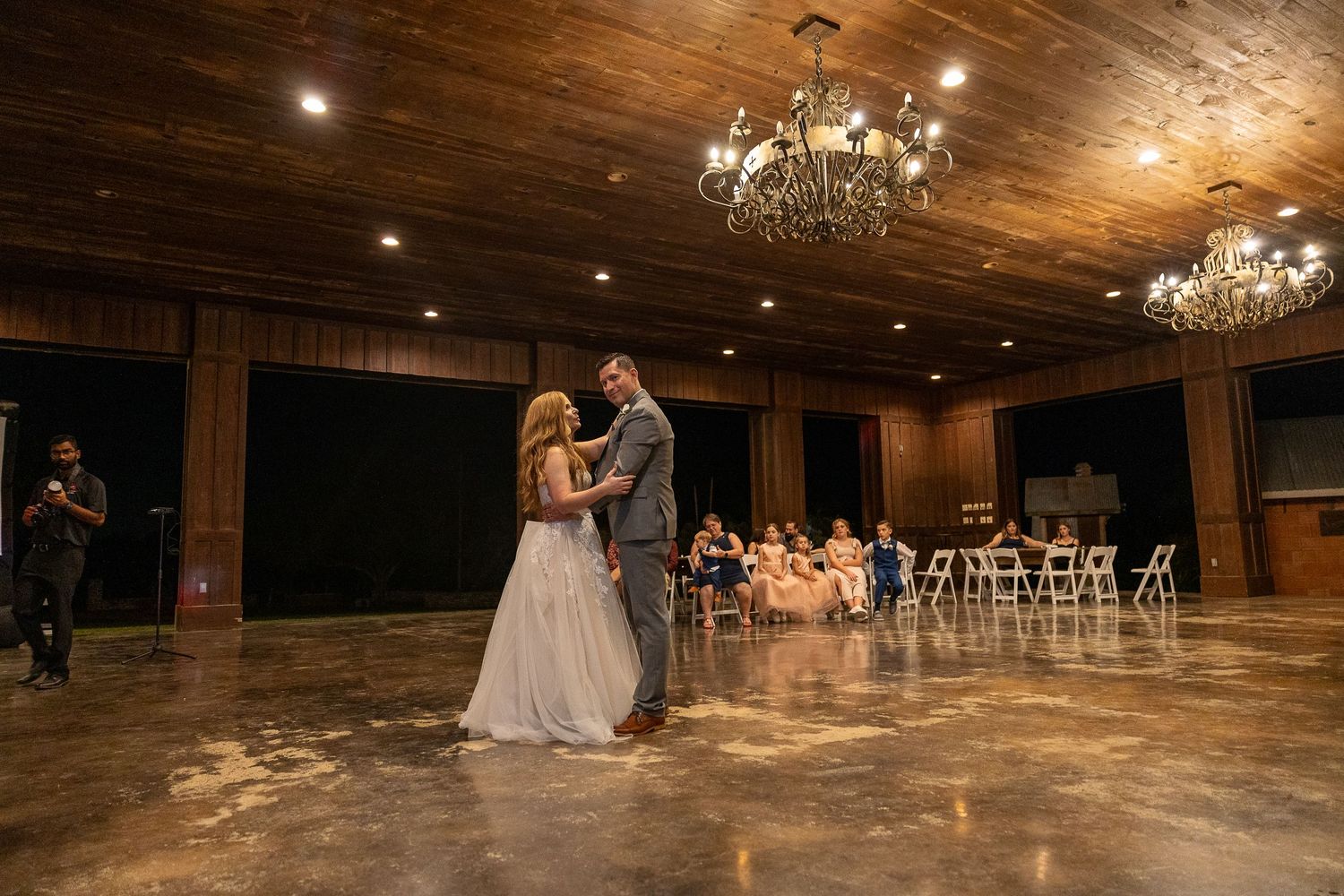 A romantic first dance in an elegant ballroom with chandeliers and wooden floors.