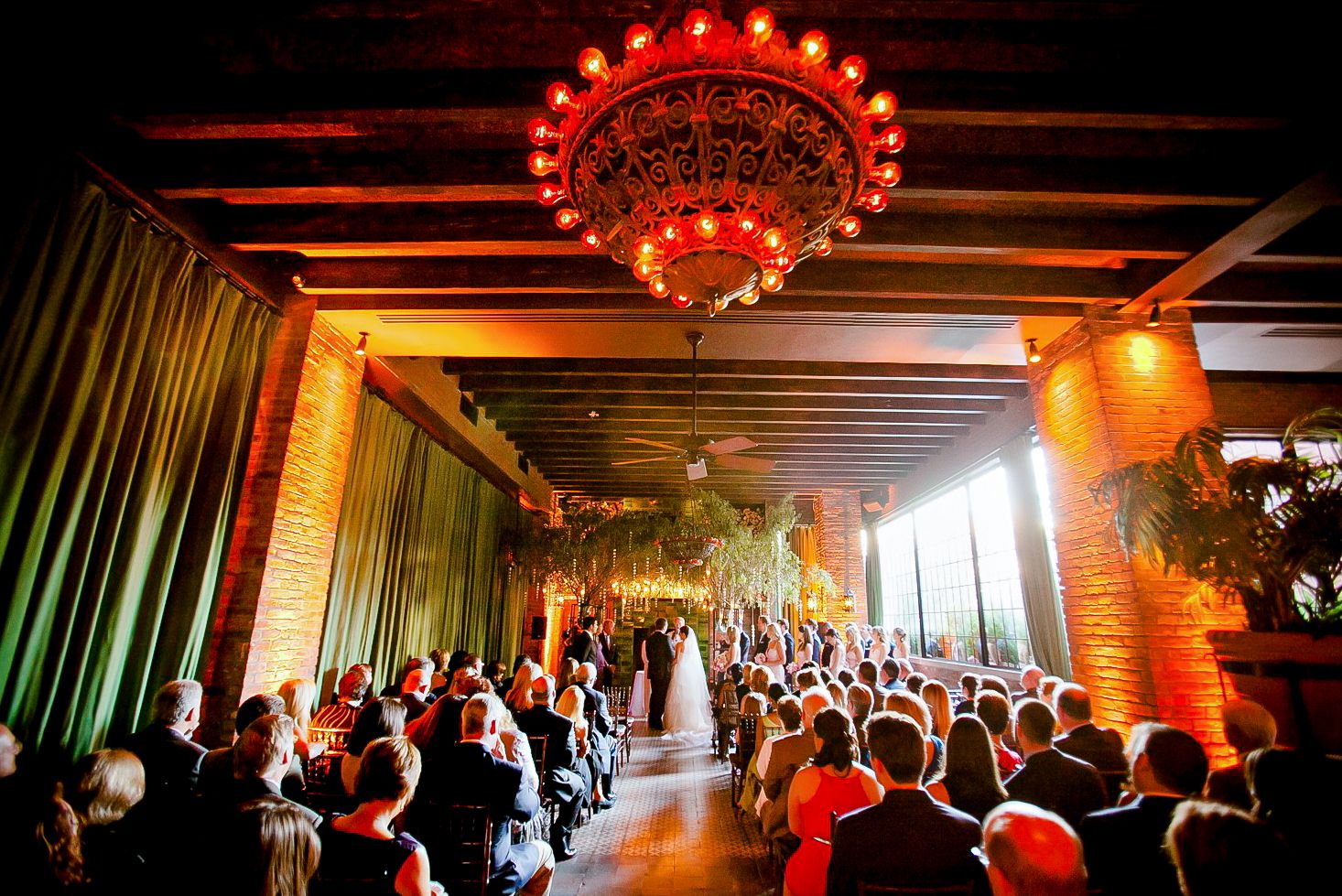 Reception venue decorated with dramatic red lighting and illuminated chandeliers during a celebration.