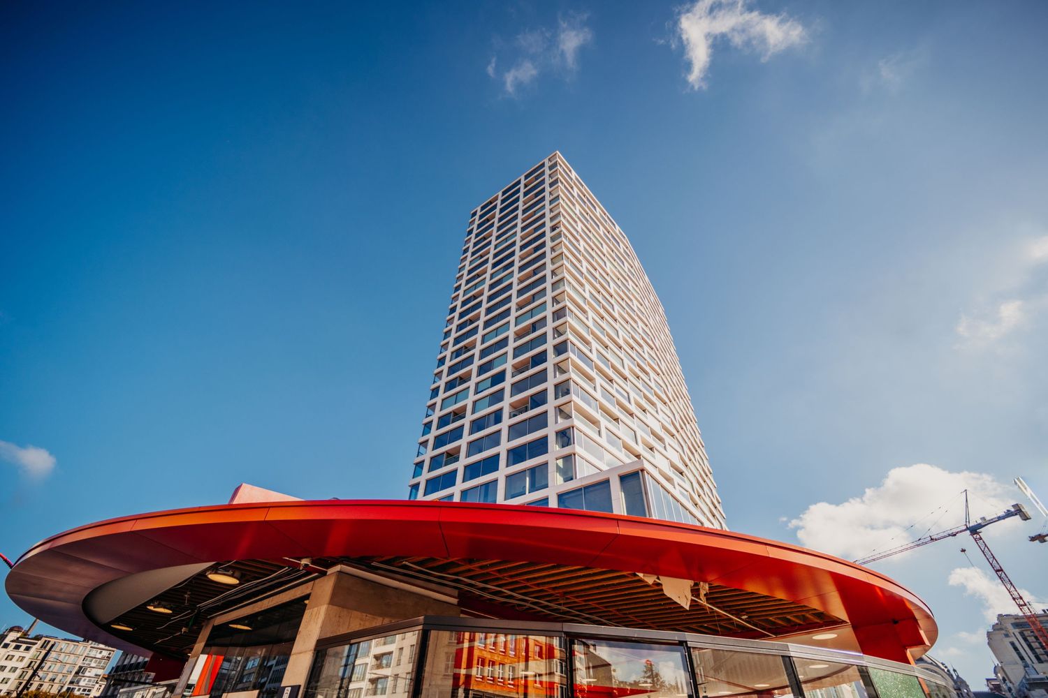 Hedendaags torengebouw met opvallende rode ronde luifel tegen blauwe lucht.