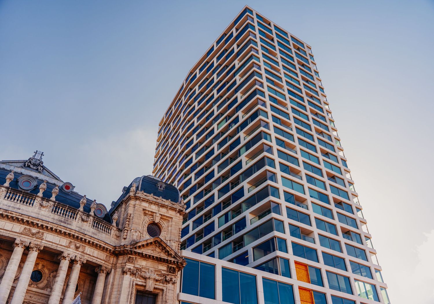 Moderne glazen toren naast historische stenen gebouwarchitectuur.