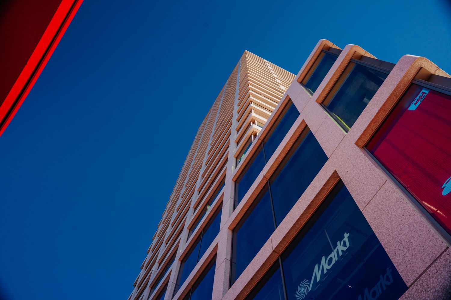 Hoekig architectonisch detail van modern gebouw met rood accent tegen diepblauwe lucht.