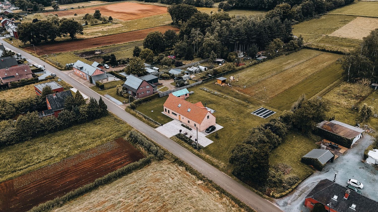 dronefoto van een landelijk landgoed met wit huis langs een weg omringd door landbouwvelden en bomen.