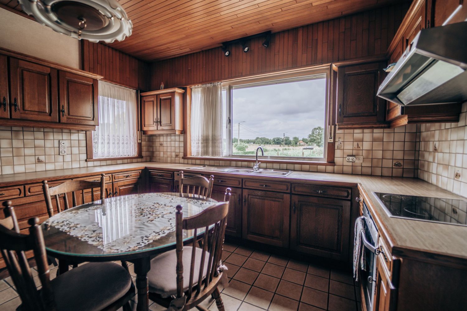 Een vintage keuken met houten kastjes, een betegelde achterwand en een groot raam met uitzicht op het buitenland.