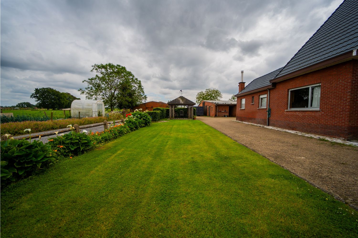 Een goed onderhouden gazon en tuin buiten een rood bakstenen huis onder een bewolkte hemel.