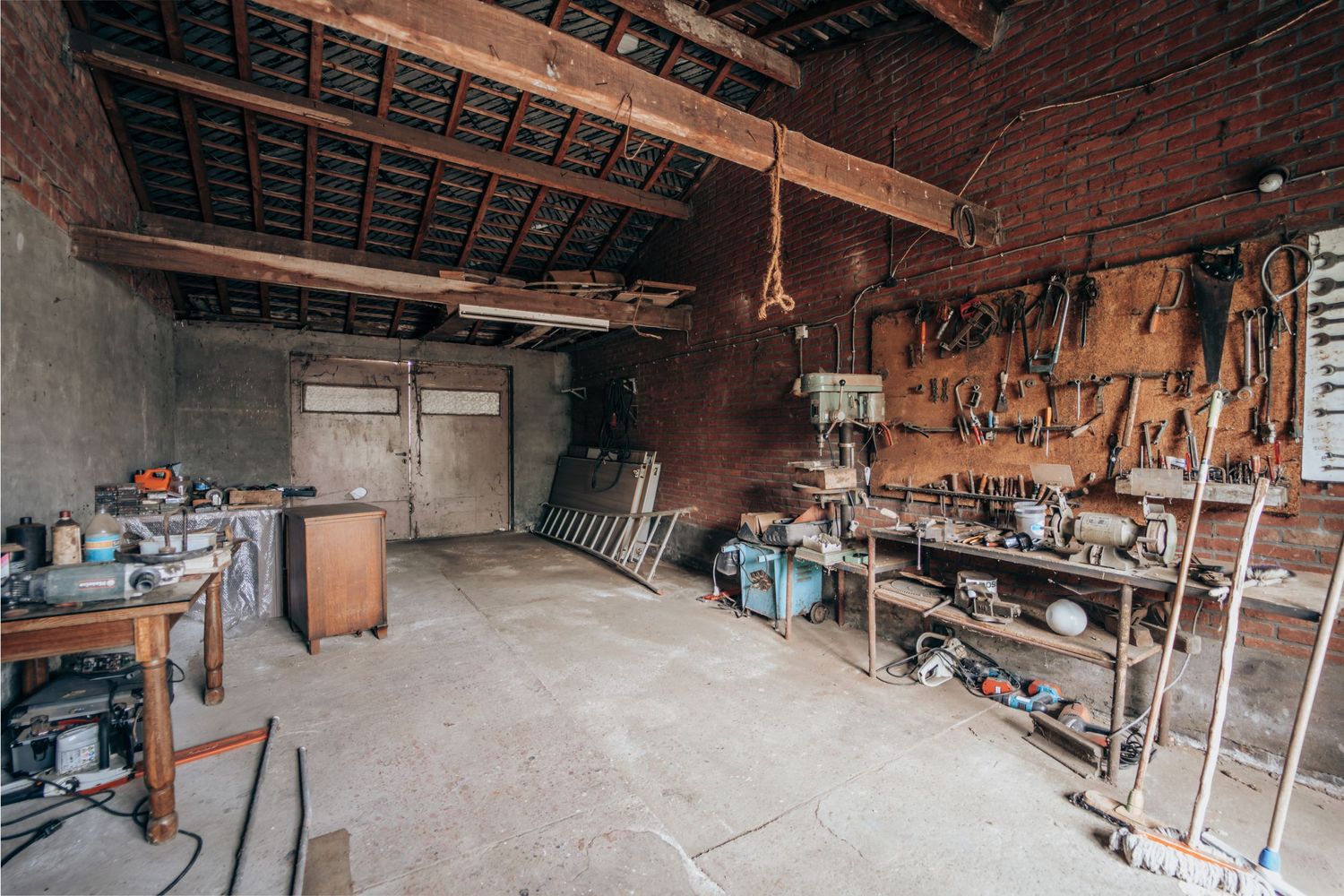 Een werkplaats of garage-interieur met gereedschap dat aan de muren hangt en diverse apparatuur die binnen is opgeborgen.