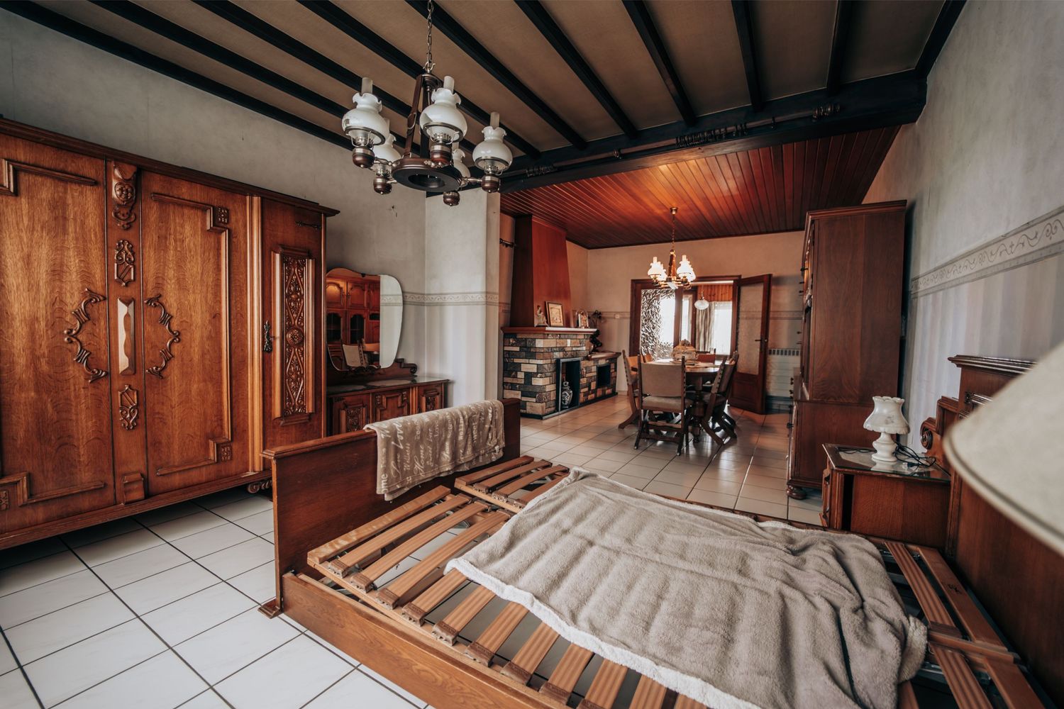 Een ruime slaapkamer met traditionele houten meubels en tegelvloeren onder zichtbare plafondbalken.