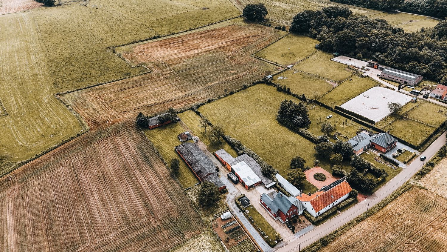 Luchtfoto van een landelijk landgoed met roodoranje gebouwen en landbouwvelden eromheen.