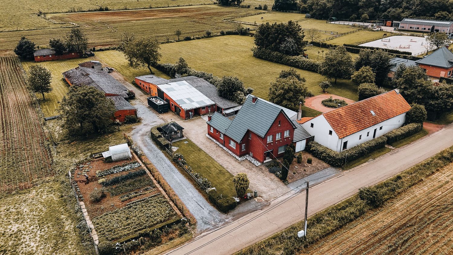 Luchtfoto van rode boerderijgebouwen en huizen langs een landweg omringd door velden.