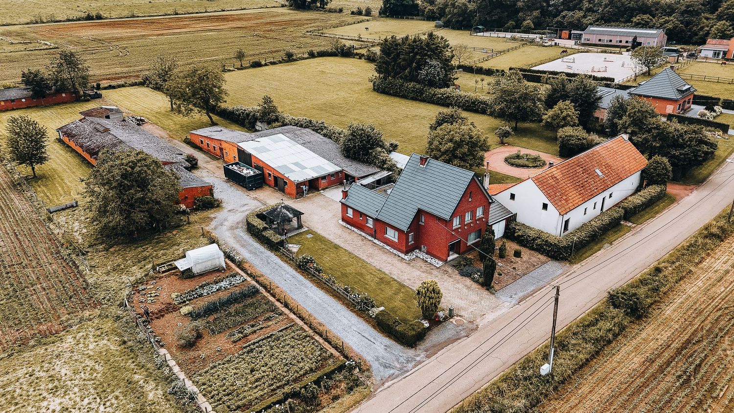 Bovenaanzicht van een landelijk landgoed met rode gebouwen en een verharde oprit te midden van landbouwgrond.