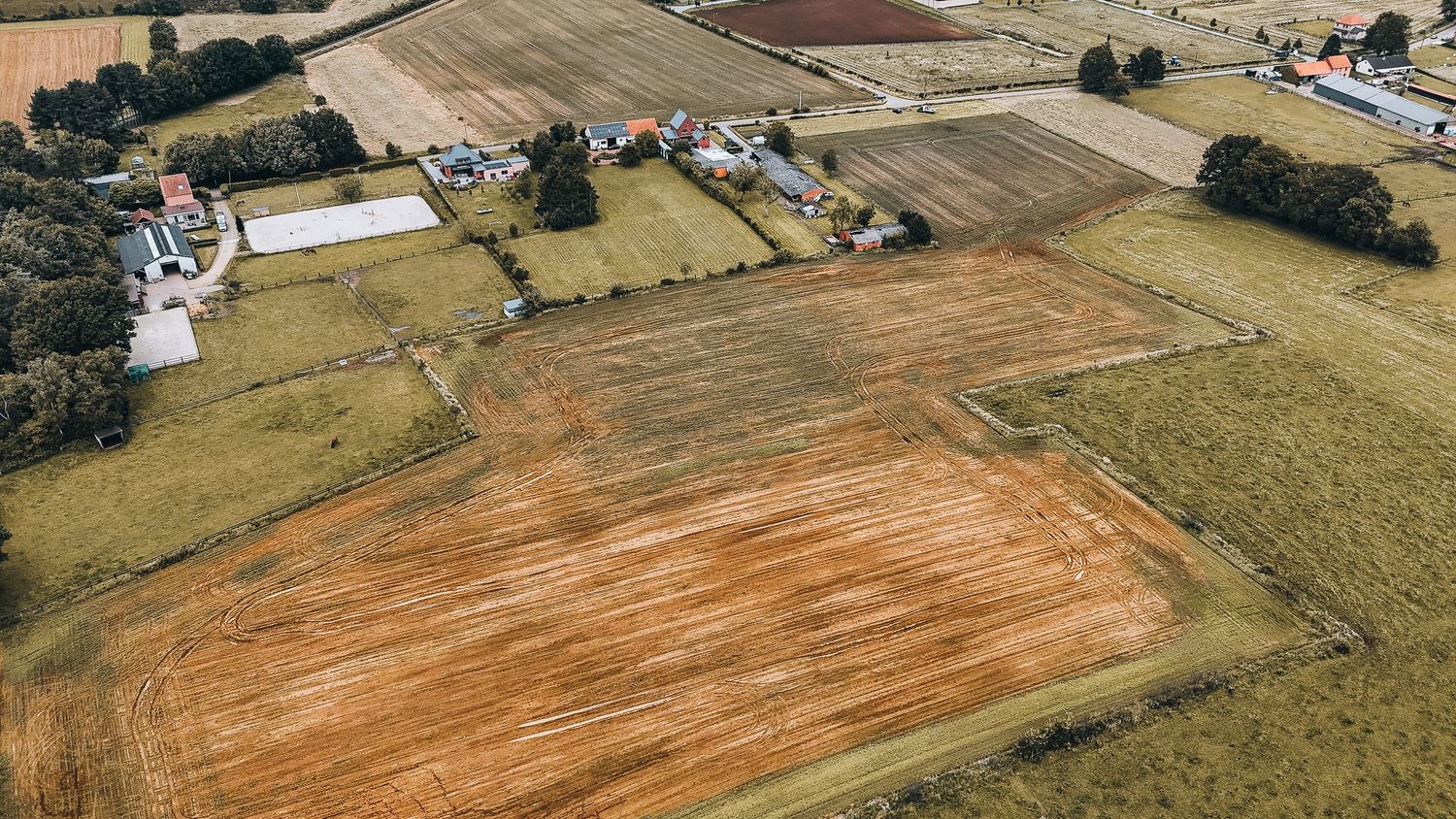Luchtfoto van geploegde landbouwvelden en verspreide boerderijgebouwen op het platteland.