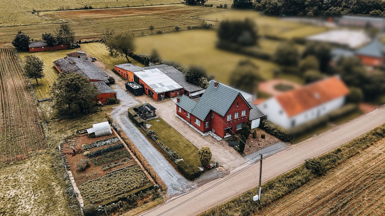 Luchtfoto van rode boerderijen en woongebouwen langs een plattelandsweg met selectieve focus.
